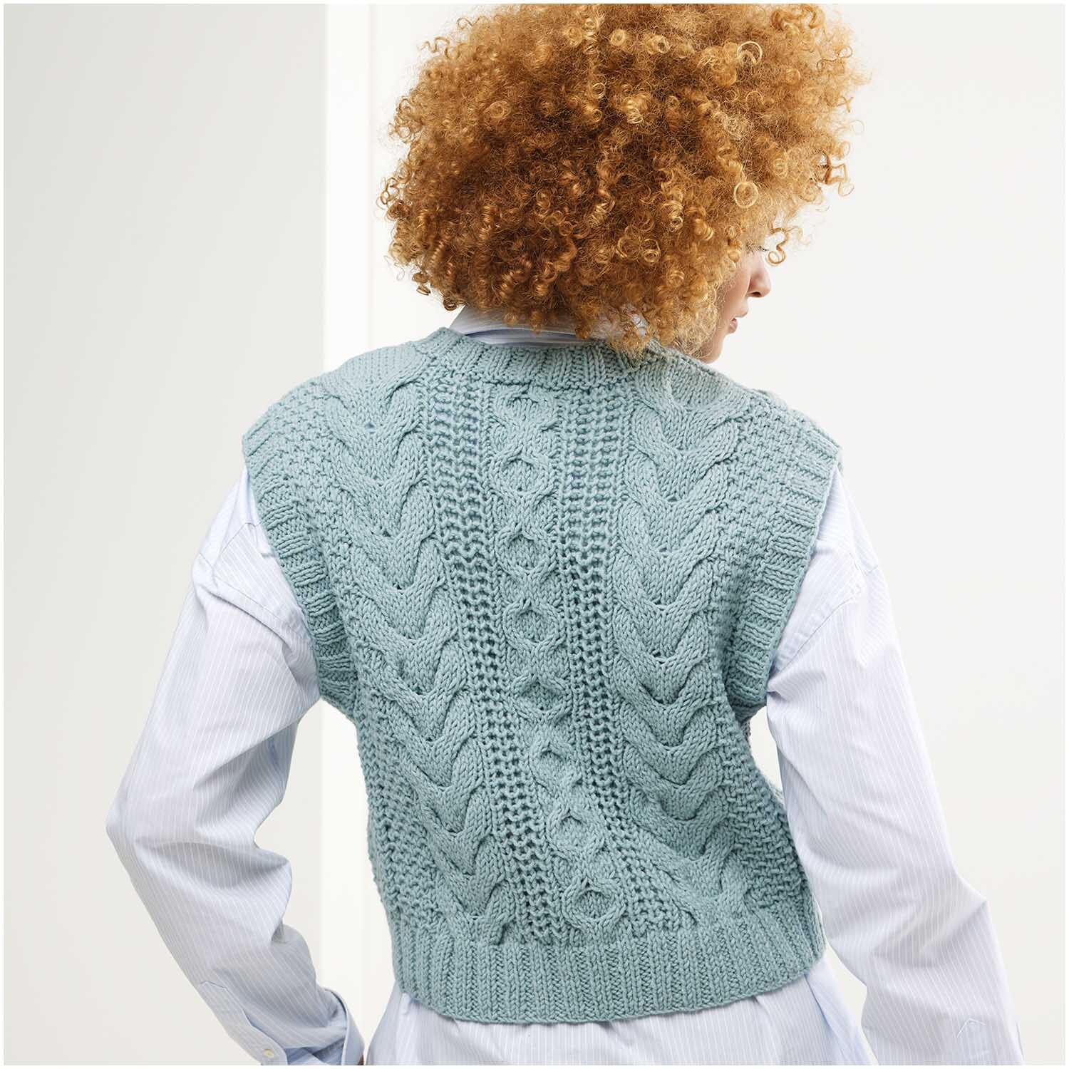 Strickset Pullunder Modell 21: Frau trägt blauen, gestrickten Pullunder mit Zopfmuster über weißem Hemd.