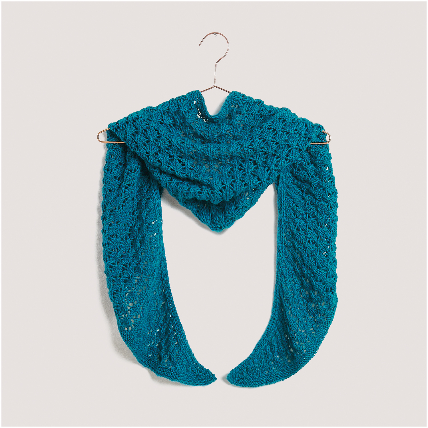 Strickset Dreieckstuch Modell 31 aus Lovewool Nr. 18 in Blau, kunstvoll drapiert auf einem Kleiderbügel.