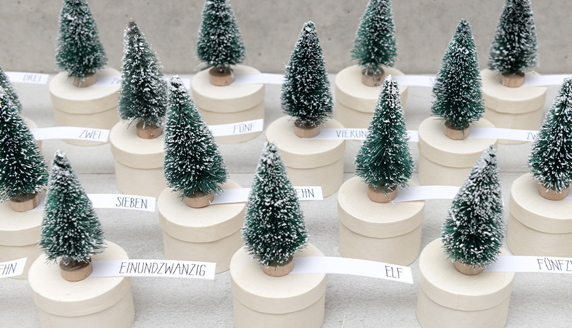 Bastelanleitung Winterwald-Adventskalender: Kleine grüne Tannenbäume auf runden, weißen Boxen.