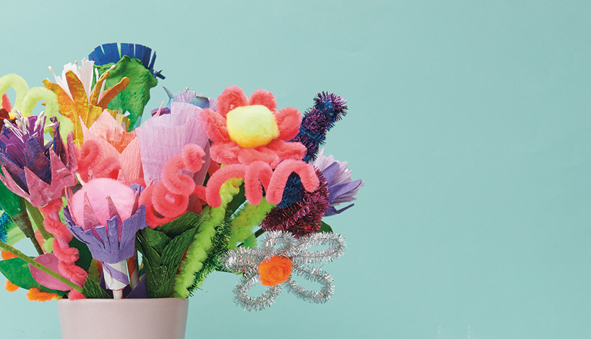 Bastelanleitung Blumen aus Eierkarton: Bunter Strauß aus Eierkartonblumen in einem weißen Topf vor blauem Hintergrund.