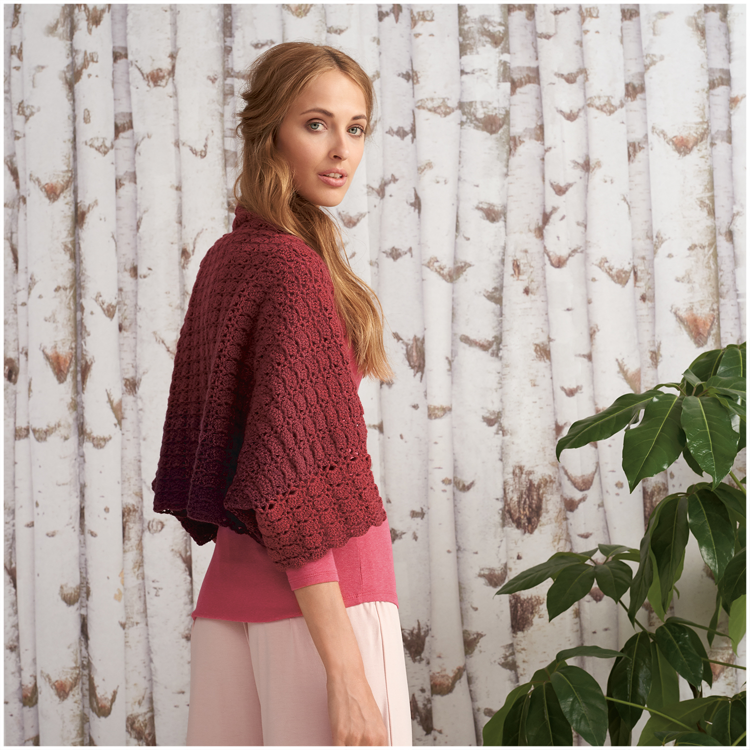 Creative Wool dégradé: Frau trägt gestricktes, rotes Cape vor Birkenwald-Hintergrund. Perfekt für stilvolle Herbstmode.