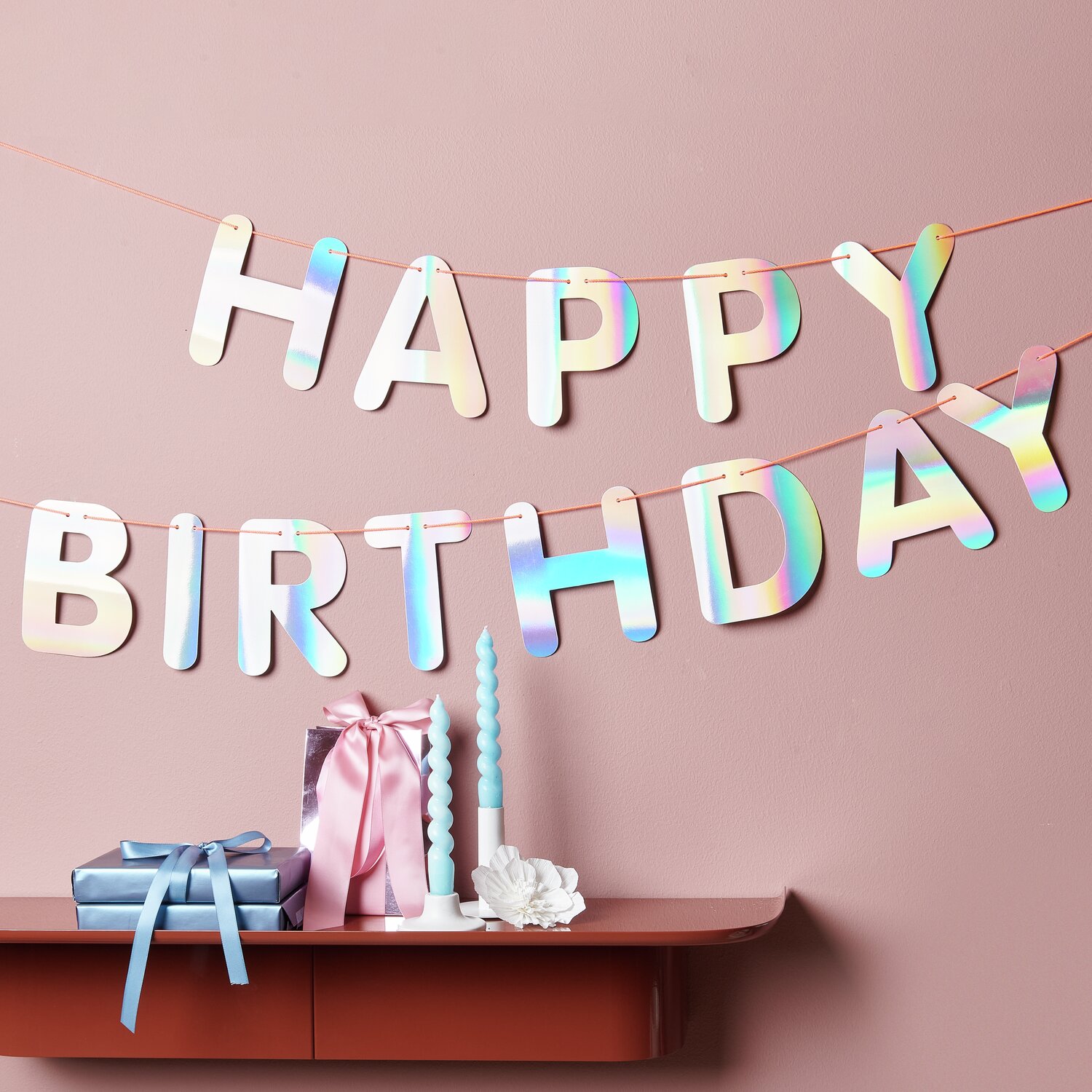 Paper Poetry Girlande mit irisierenden Buchstaben "Happy Birthday" von Rico Design, dekoriert auf einem Tisch mit Geschenken und Kerzen.
