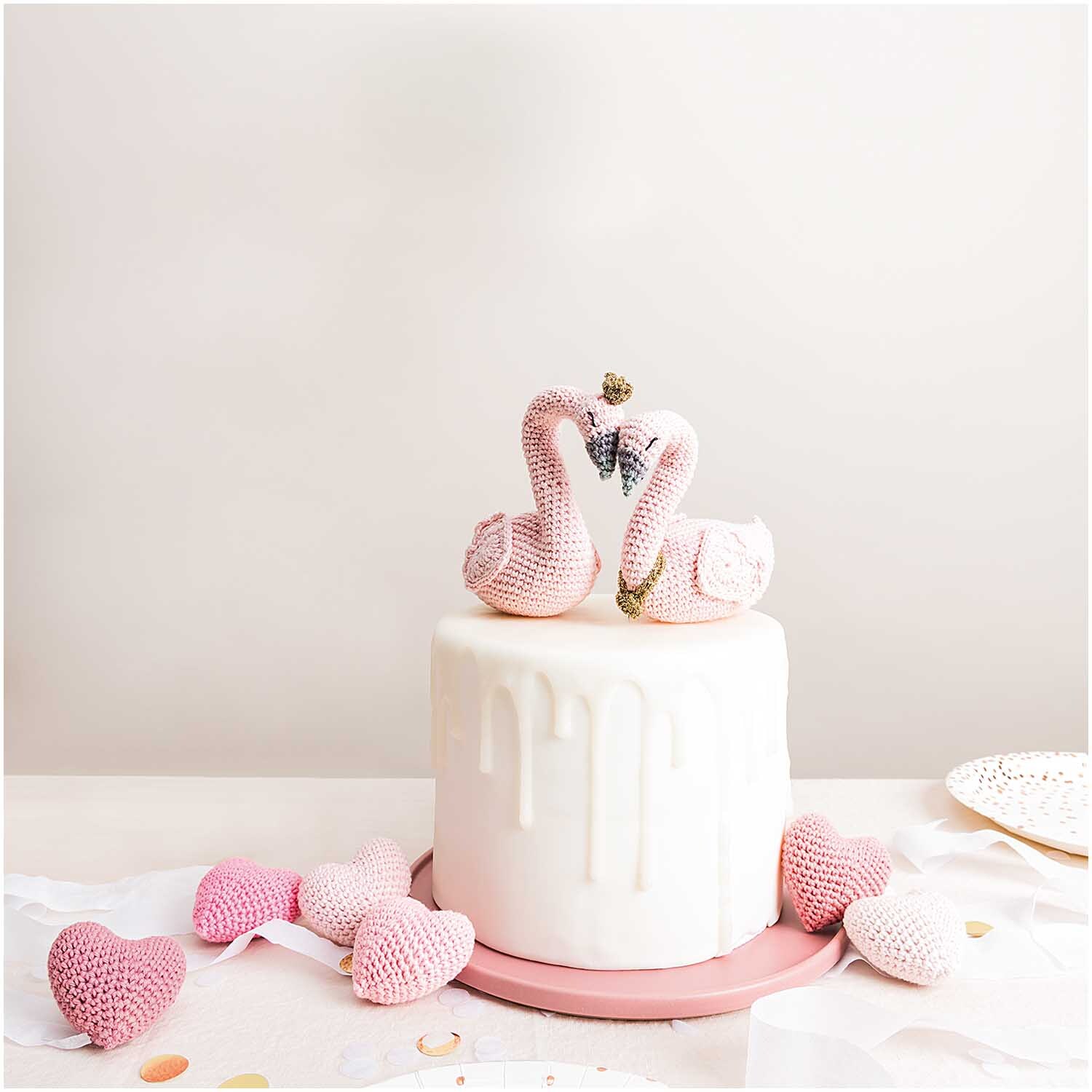 Creative Ricorumi dk: Zwei gehäkelte rosa Schwäne auf einer weißen Torte, umgeben von rosa Herzen. Ideal für kreative Dekorationen.
