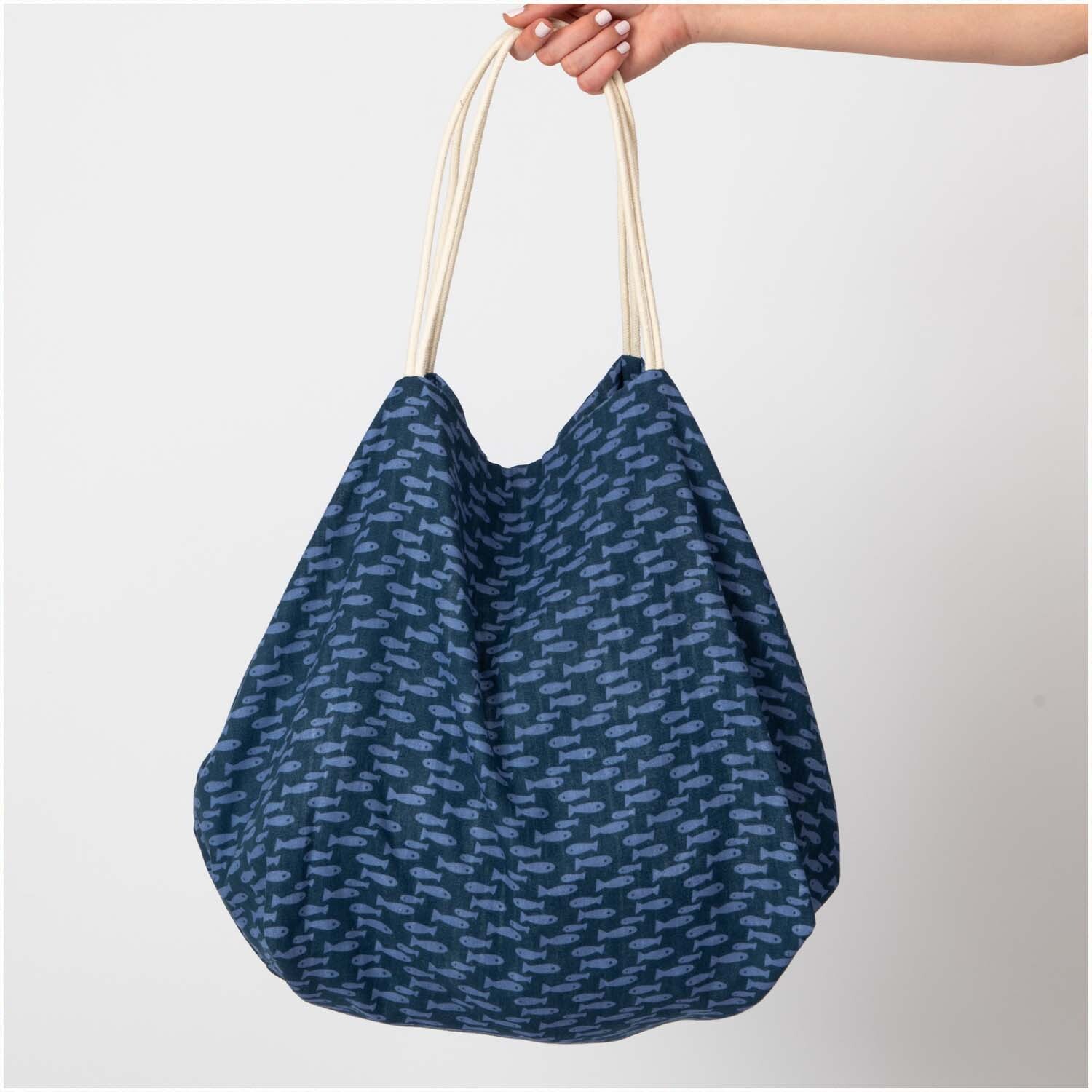 Musselin-Druckstoff Mermaid Fische: Eine blaue Tasche mit Fischmuster, gehalten von einer Hand.
