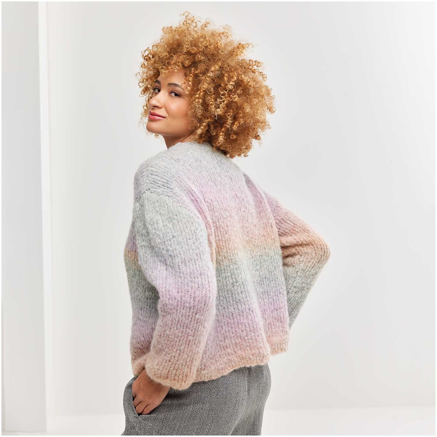Strickset Pullover Modell 12 aus Die Neue Masche Nr. 7: Frau trägt pastellfarbenen, gestrickten Pullover, lächelt über die Schulter.