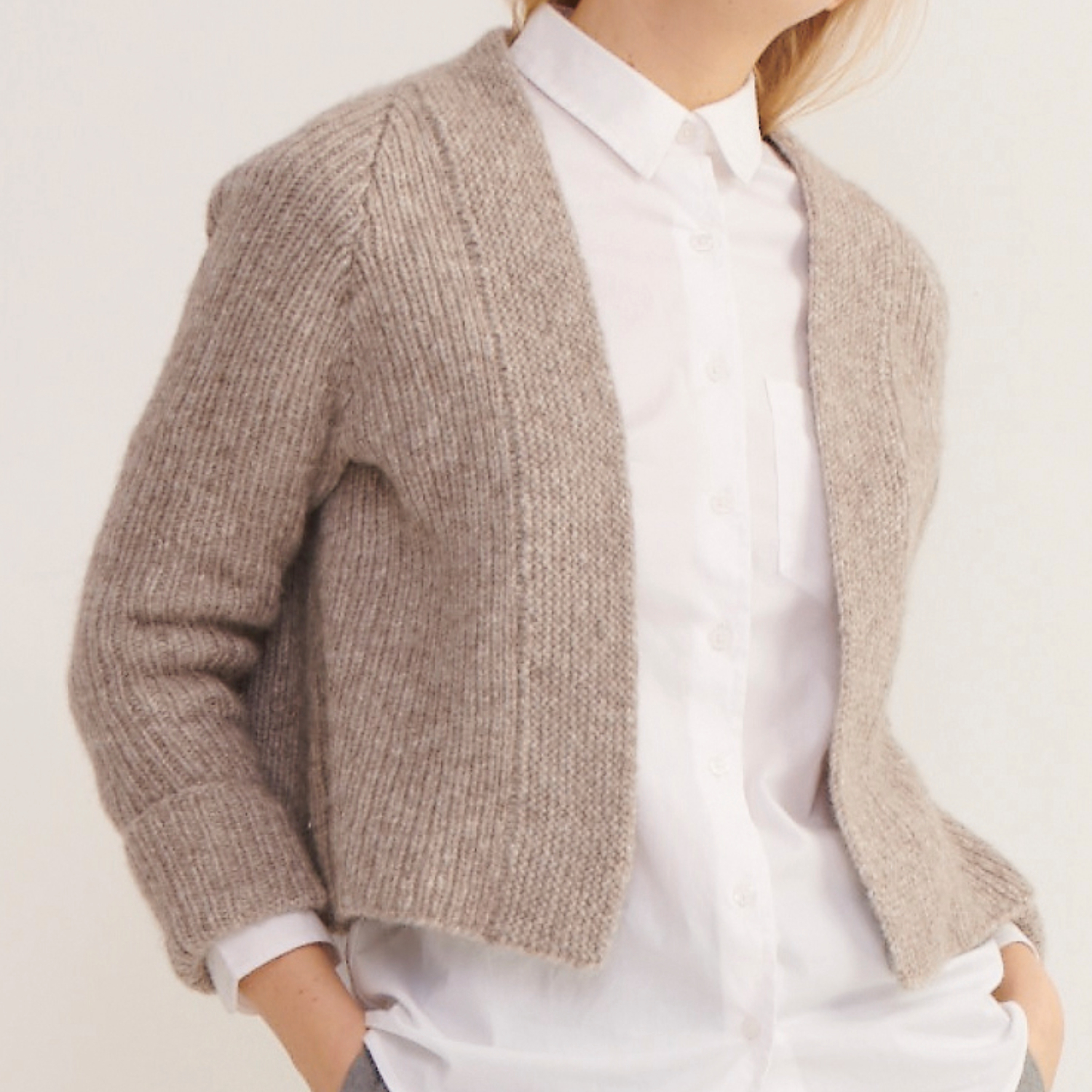 Strickanleitung Jacke aus Alpaca Superfine aran: Beigefarbene Strickjacke über weißem Hemd, elegant und gemütlich.
