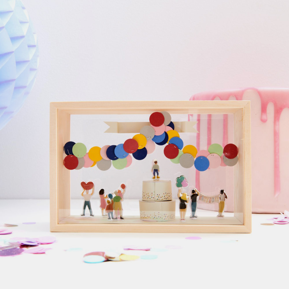 Objektkasten mit gebastelter Torte, bunter Luftballon-Girlande und verschiedenen Mini-Figuren.