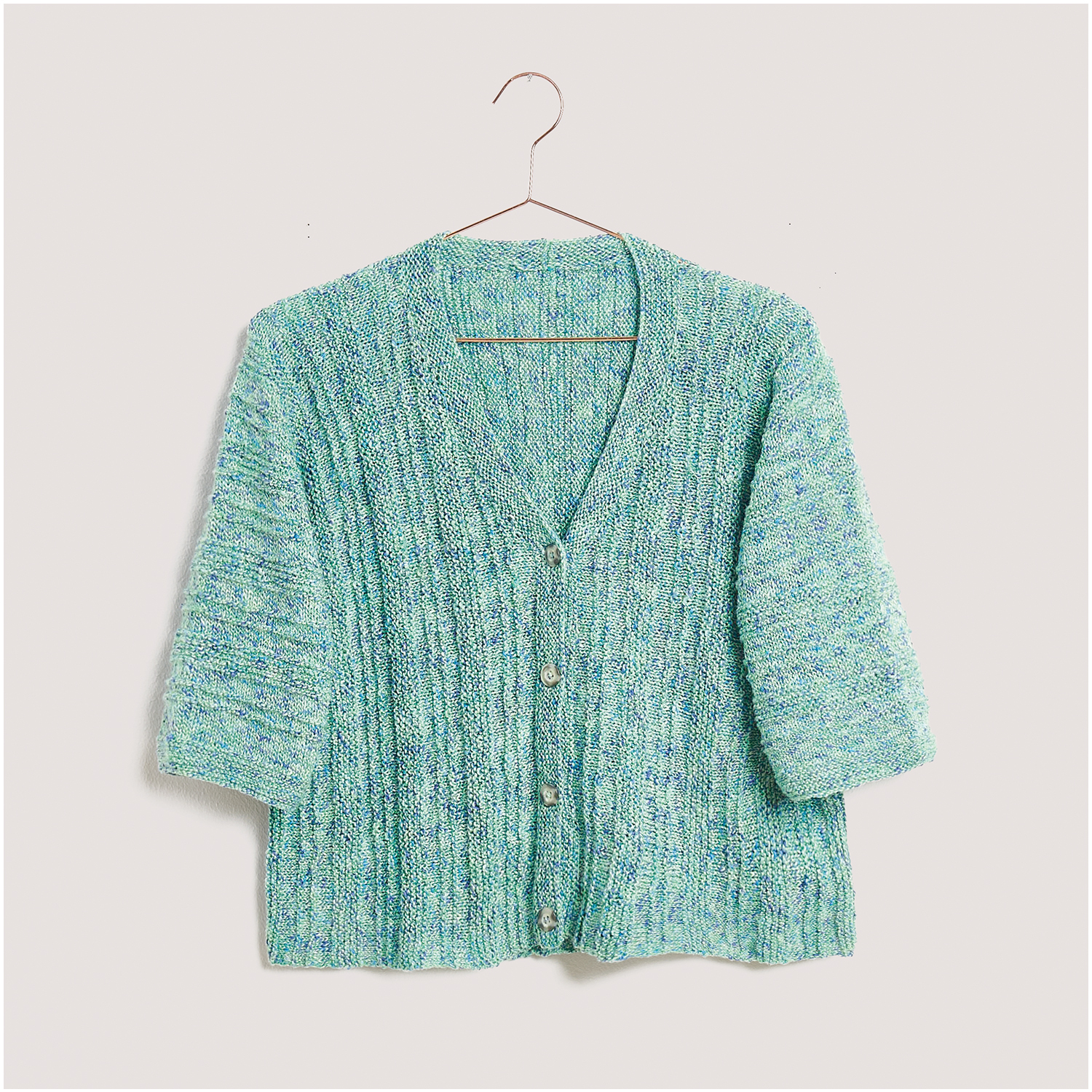 Strickset Jacke Modell 24 aus Lovewool Nr. 18: Eine gestrickte, hellblaue Jacke mit V-Ausschnitt und Knöpfen, auf einem Kleiderbügel präsentiert.