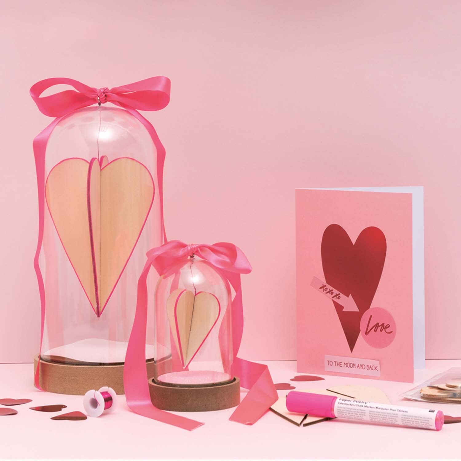 Bastelanleitung Dekohaube mit Steckherzen: Zwei Glasglocken mit rosa Bändern und Herzdeko.