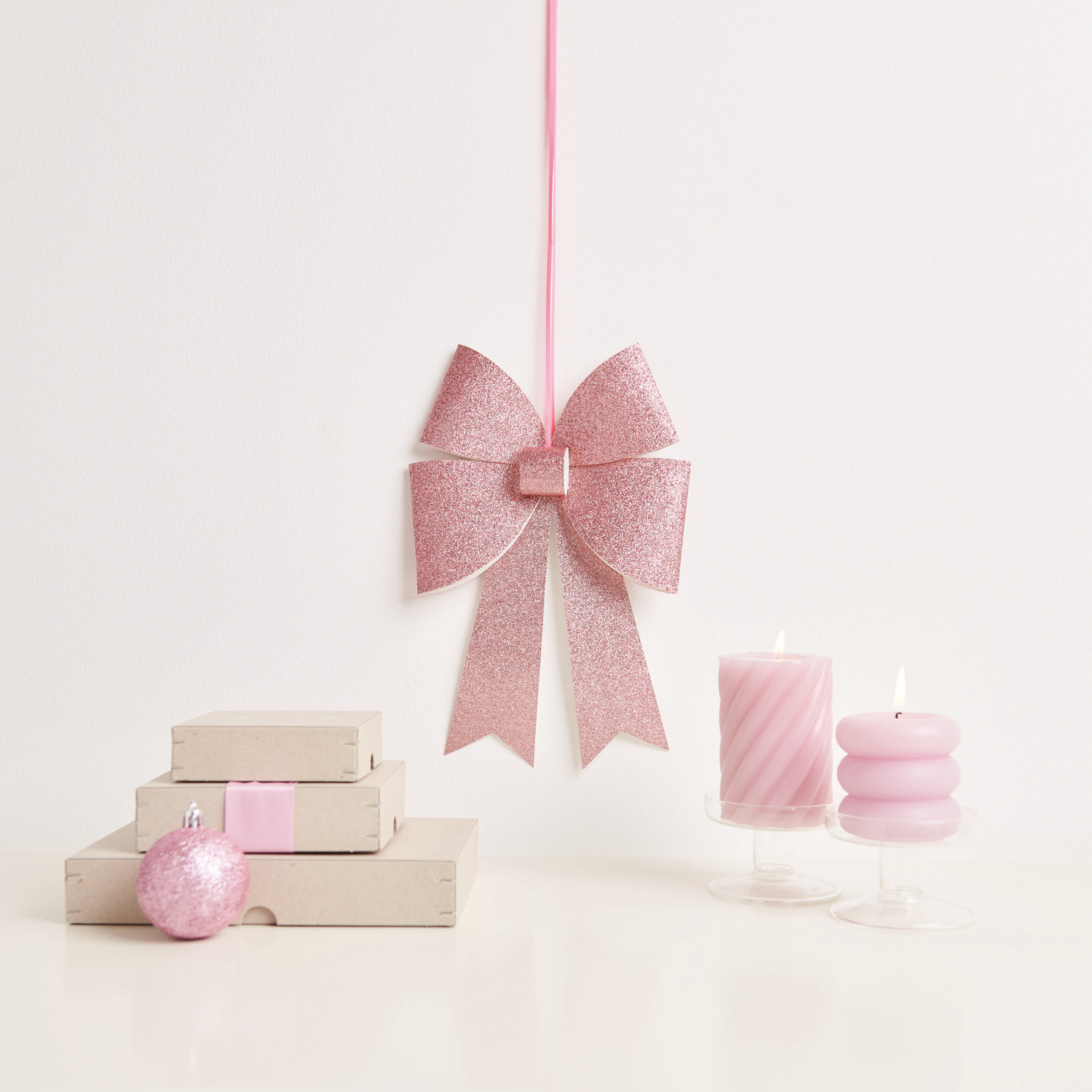 Paper Poetry Bastelset XL-Schleife Glitter zeigt eine funkelnde Schleife neben rosa Kerzen und Dekoration. Ideal für kreative Projekte.