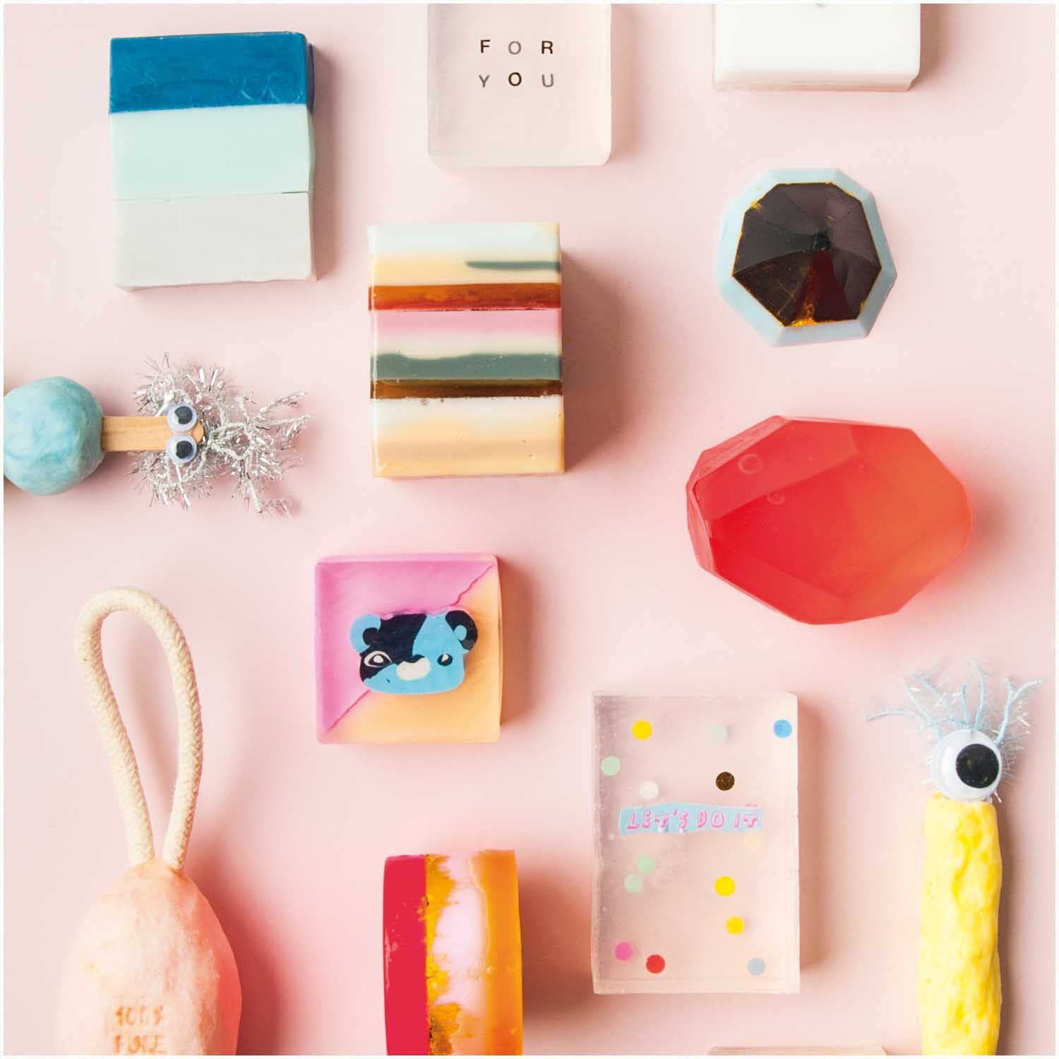 Seifengießform quadratisch von Rico Design in einem kreativen Arrangement mit bunten Seifen und Accessoires auf rosa Hintergrund.