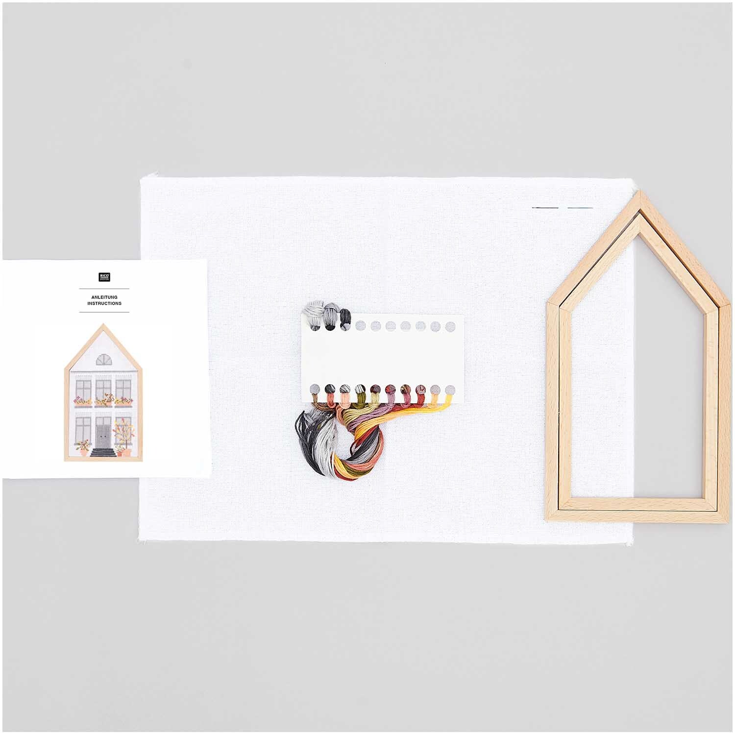 Stickpackung Herbsthaus mittel 12x22,5cm von Rico Design zeigt ein Set mit Garn, Stoff und Holzrahmen in Hausform für kreative Stickprojekte.