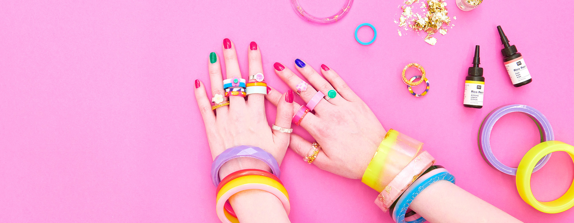 Hände mit bunten Ringen und Armreifen und Resin. Fotosetting graue Ecke.