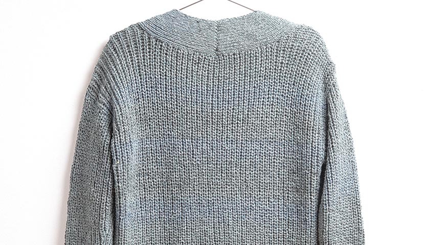 Strickanleitung Cardigan aus Fashion Cotton Light & Long Tweed dk: Rückansicht eines grauen, grob gestrickten Cardigans auf einem Kleiderbügel.