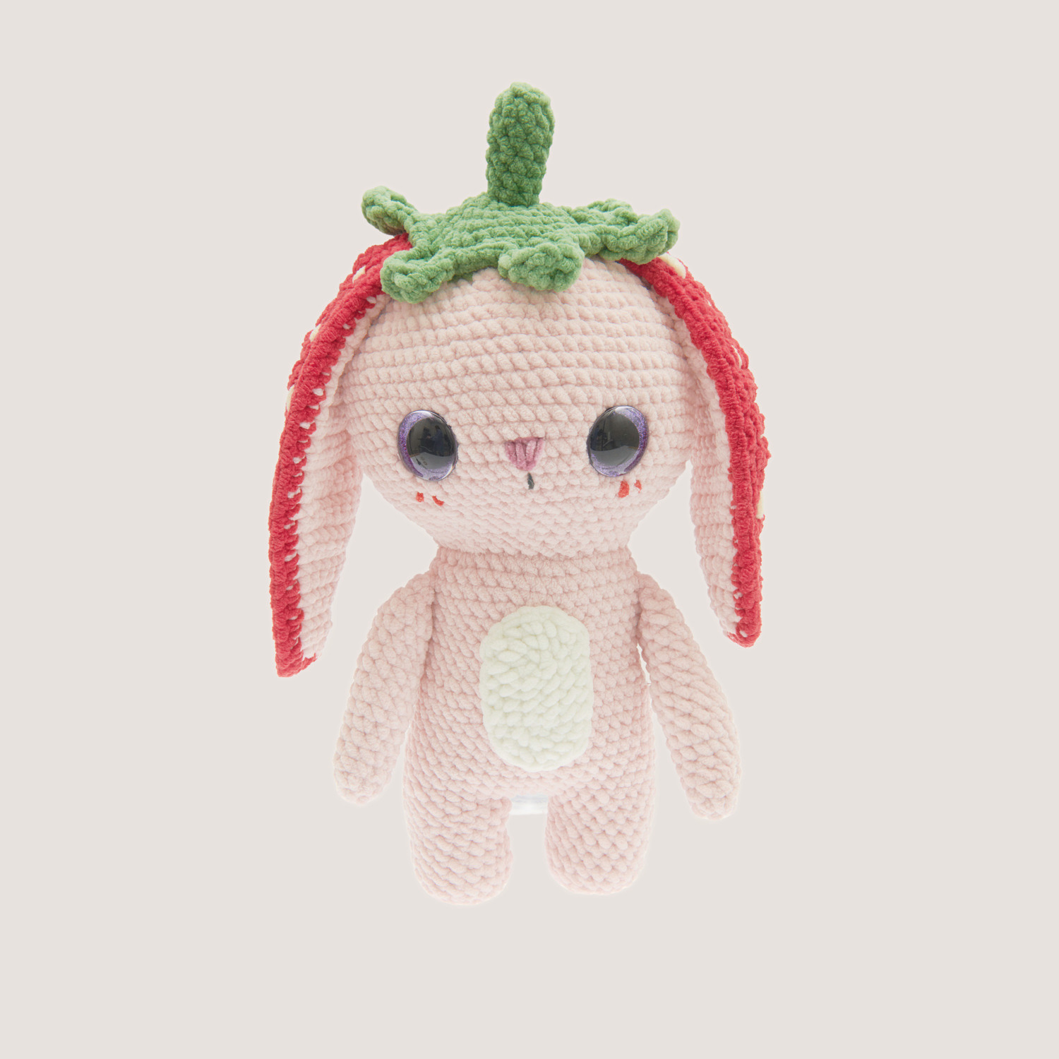 Häkelset Strawberry Bunny Modell 03: Ein rosa gehäkelter Hase mit Erdbeerhut und großen Augen.