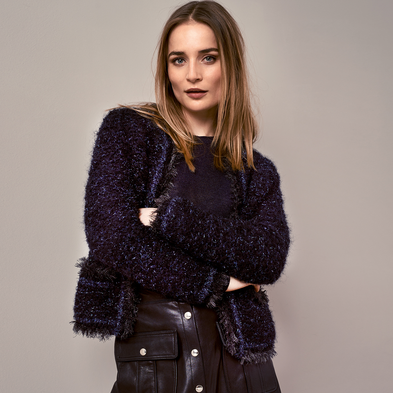 Strickanleitung Jacke in Bouclé-Optik: Frau trägt eine stilvolle, dunkle Bouclé-Jacke, kombiniert mit einer schwarzen Lederhose.