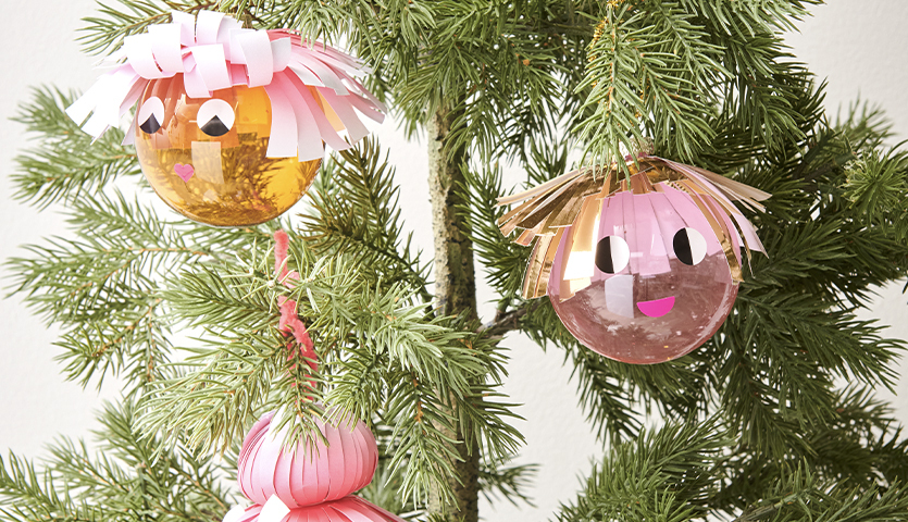 Bastelanleitung Poppige Christbaumkugeln: Bunte Kugeln mit Gesichtern und Papierfransen an einem Tannenbaum.
