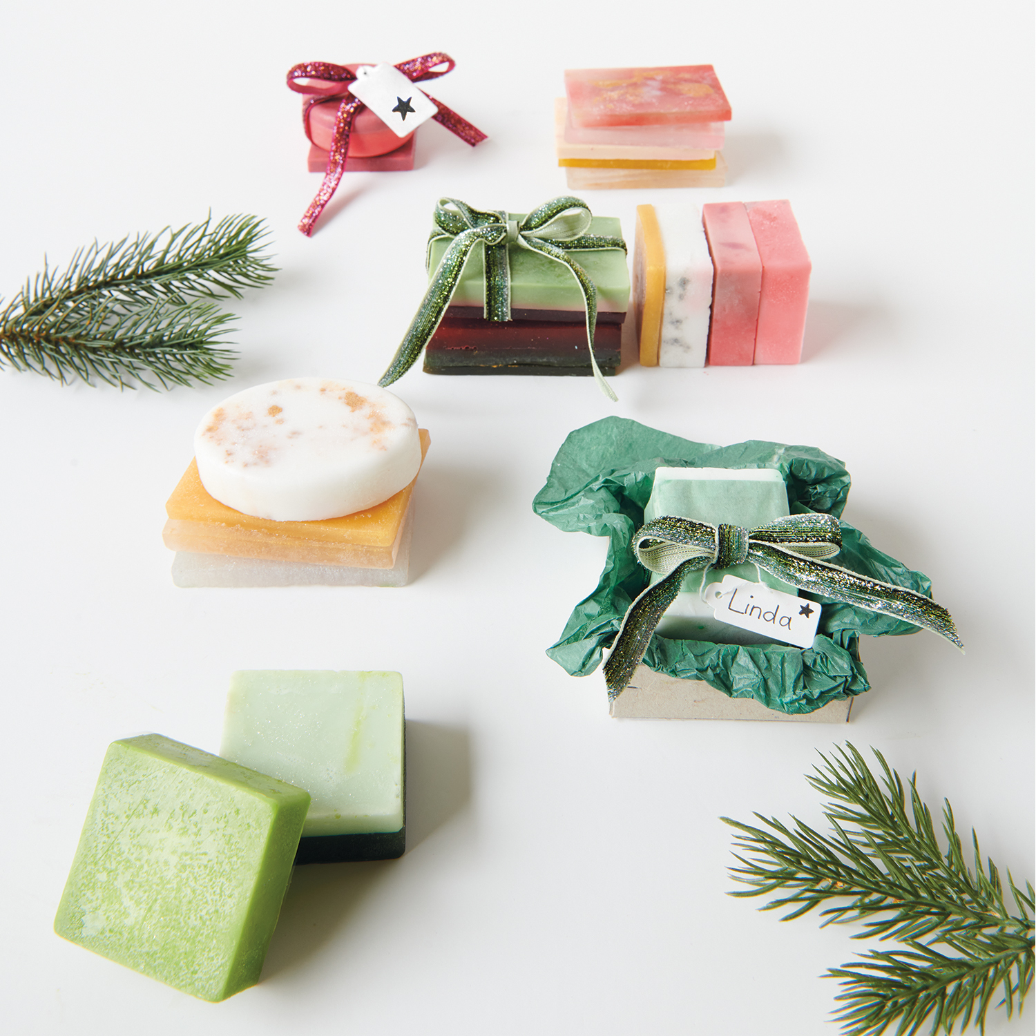 Anleitung Seife gießen und weihnachtlich verpacken: Verschiedene bunte Seifenstücke, festlich dekoriert mit Schleifen und Tannenzweigen.