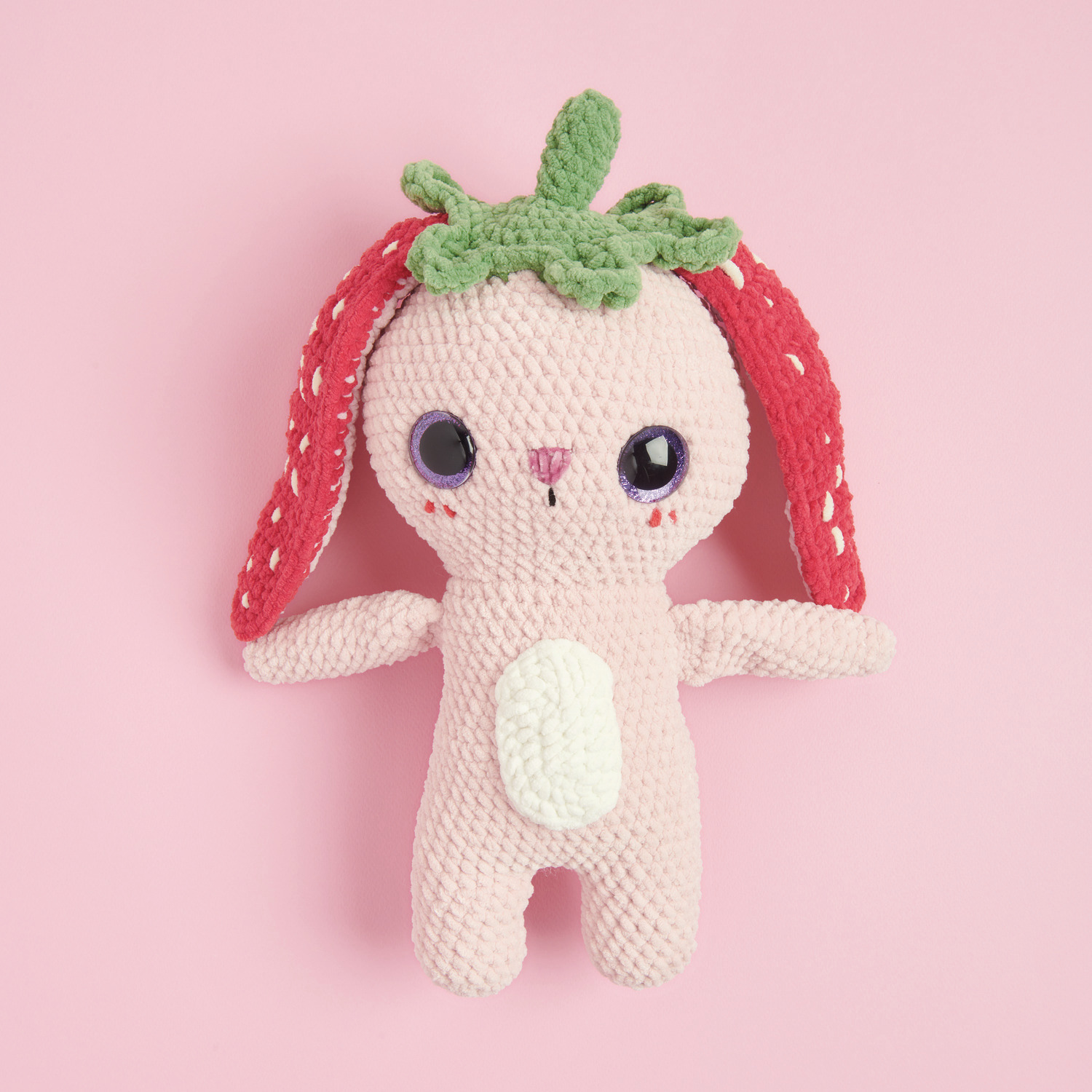 Häkelset Strawberry Bunny Modell 03: Rosa Hase mit Erdbeerohren und grüner Mütze auf rosa Hintergrund.
