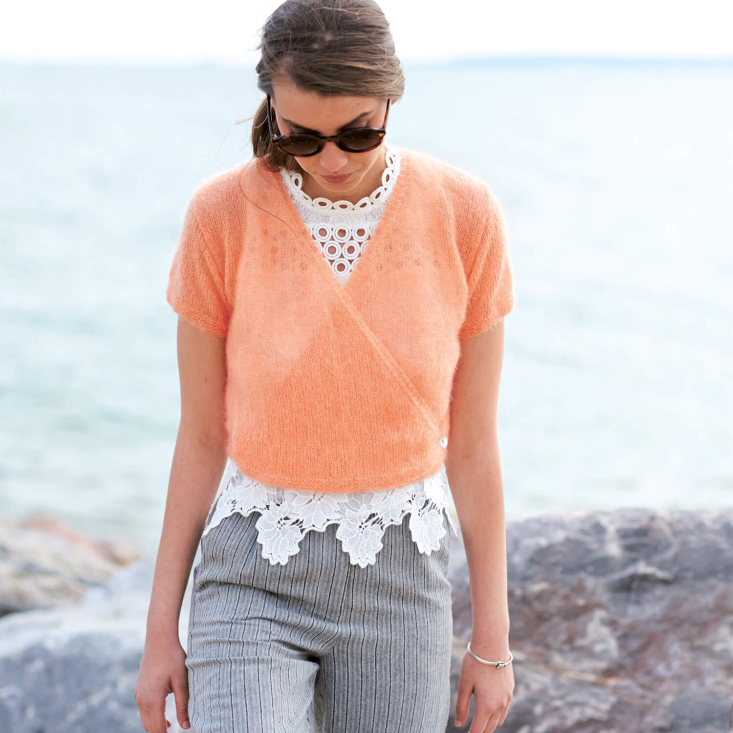 Strickanleitung Pullover in Wickeloptik: Frau am Strand trägt einen orangefarbenen Pullover aus Mohair-Seide über einem Spitzenoberteil.