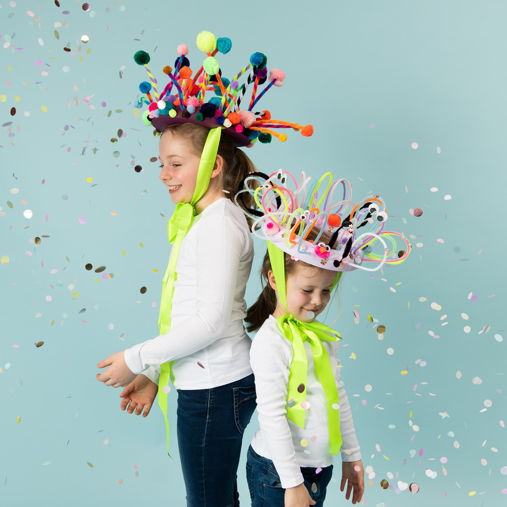 Bastelanleitung kunterbunte Karnevalskronen: Zwei Kinder tragen bunte Kronen mit Pompons und Bändern, umgeben von Konfetti.