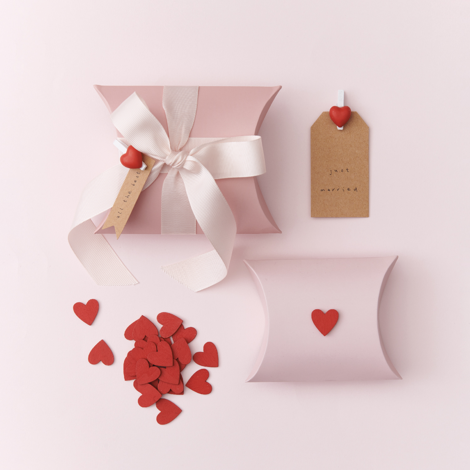 Zwei rosa Geschenkschachteln, eine mit Schleife und rotem Herz, die andere nur mit rotem Herz in der Mitte. Flatlay von Produkten.