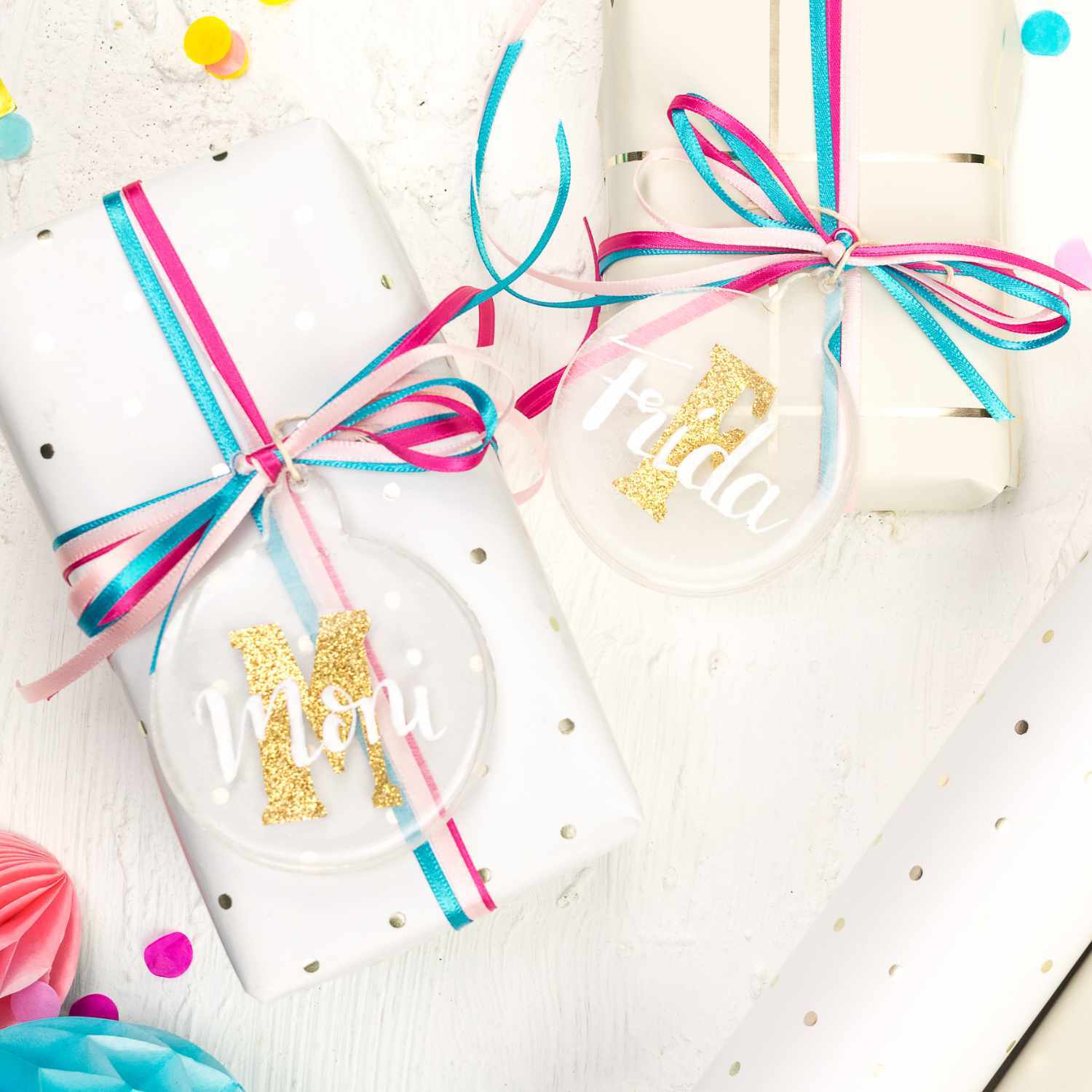 Bastelanleitung Geschenkanhänger aus Resin: Zwei weiße Geschenke mit bunten Bändern und personalisierten Resin-Anhängern.