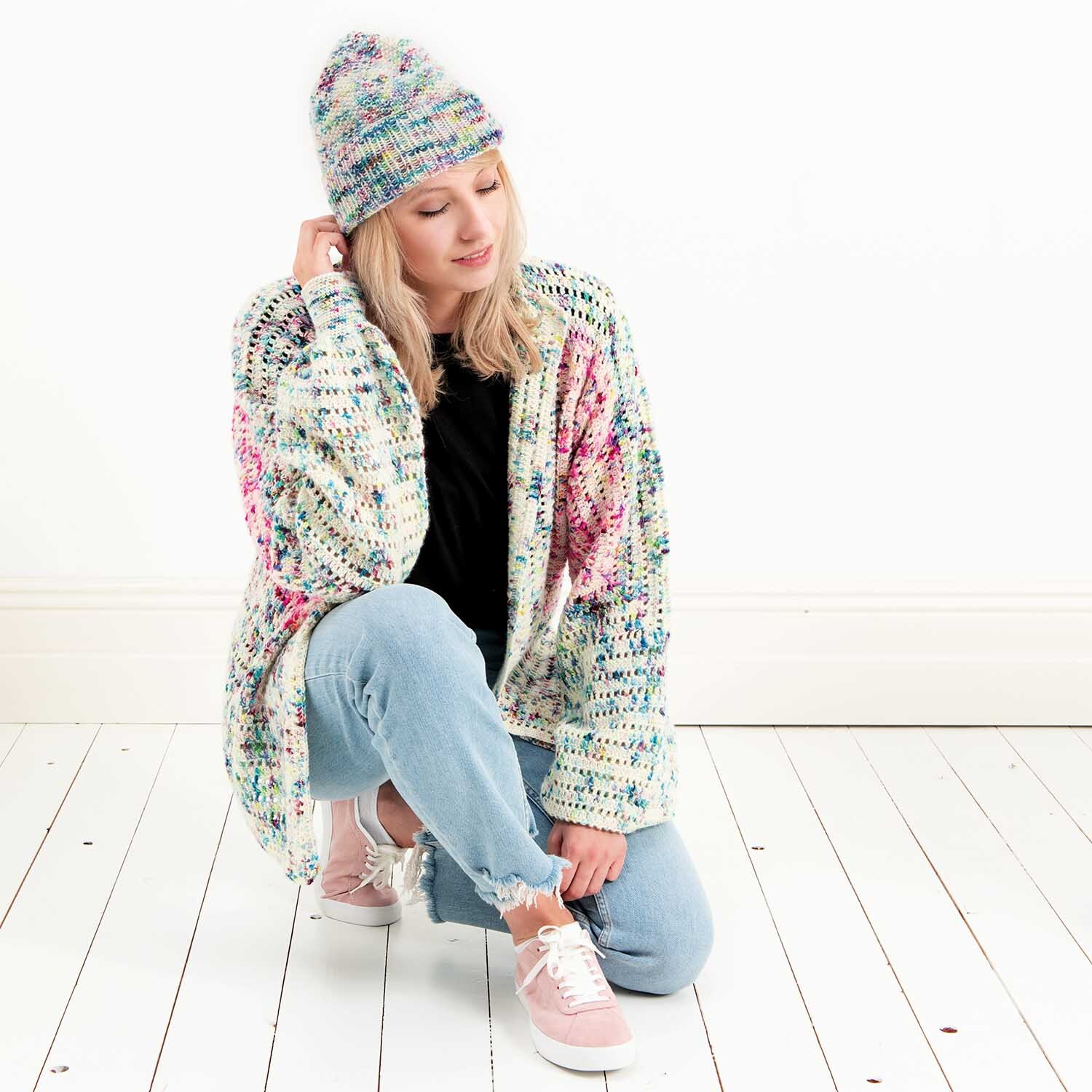Luxury Hand-Dyed Happiness dk: Frau in gestrickter Mütze und Cardigan von Rico Design auf hellem Holzboden.
