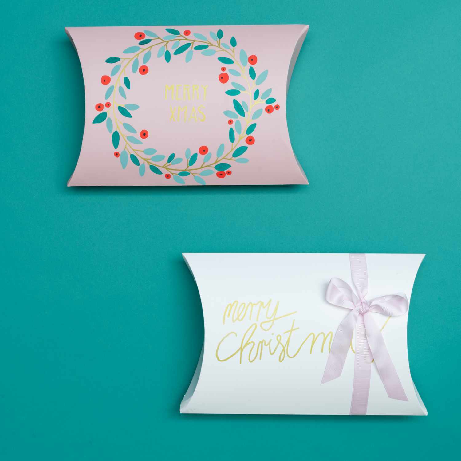 Anleitung Geschenkschachteln mit Kreidemarkern gestalten: Zwei dekorierte Schachteln auf blauem Hintergrund, eine mit Blumenkranz, die andere mit Schleife.