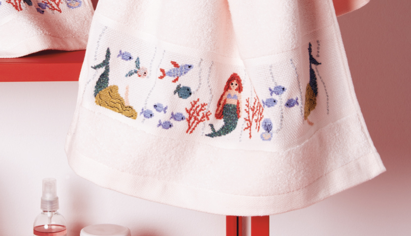 Stickanleitung Handtuch mit Meerjungfrau, Fischen und Korallen auf weißem Stoff, ideal für kreative Projekte.