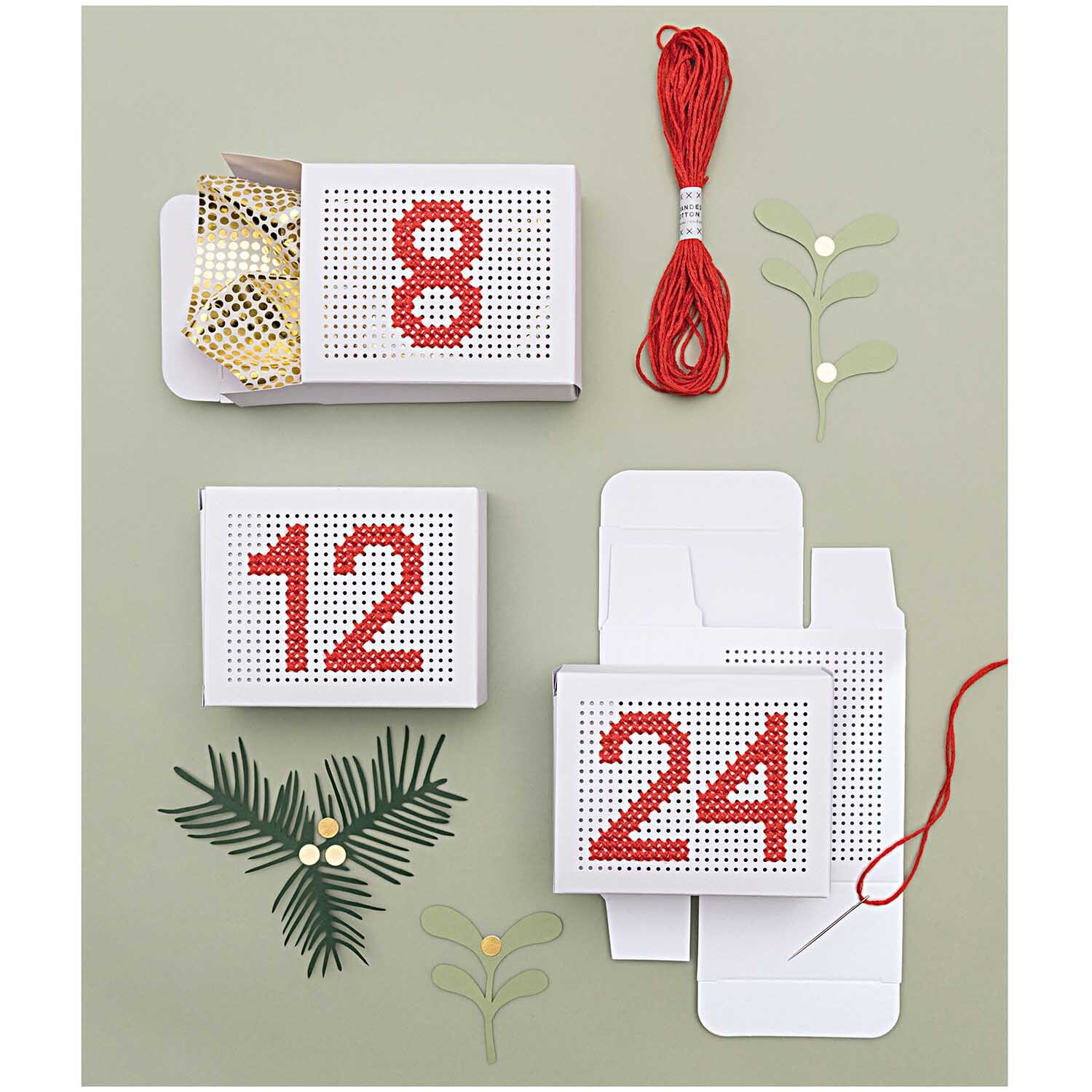 Paper Poetry Adventskalender Boxen zum Besticken von Rico Design, dekoriert mit roten Zahlen und Garn auf grünem Hintergrund.