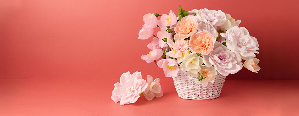 Viele verschiedenen Papierblumen in rosa Tönen in einem weißen geflochtenen Korb. Produkte aus der Kollektion La Vie en Rose.