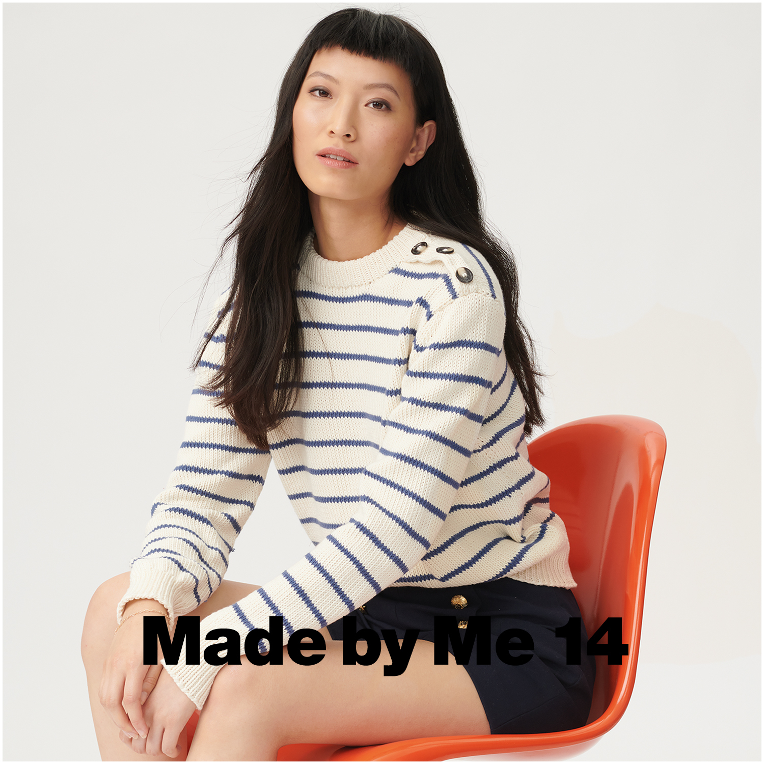Essentials Organic Cotton aran Pullover in Creme mit blauen Streifen, getragen von einer Frau auf einem roten Stuhl.