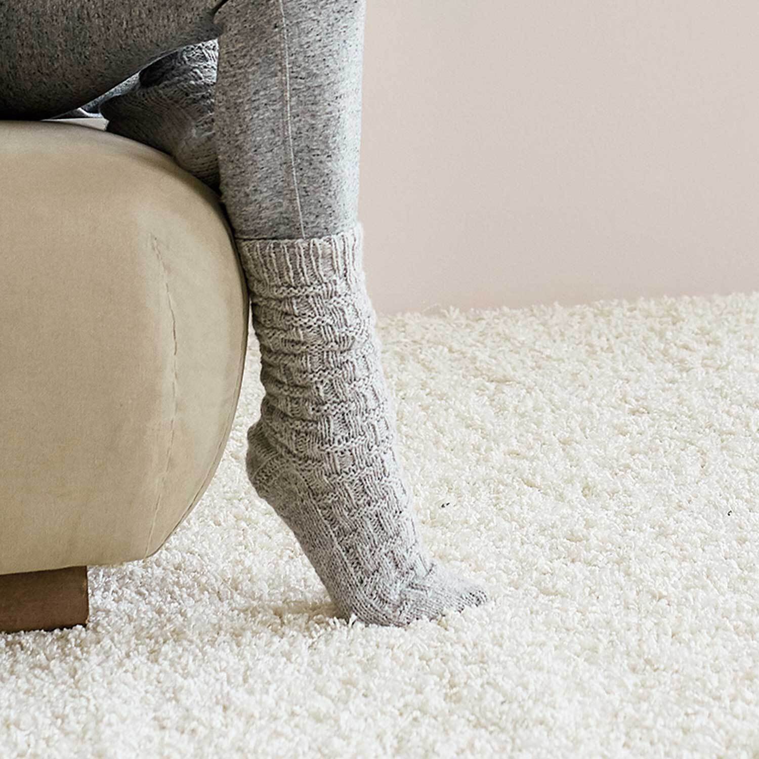 Strickanleitung Wellnesssocken: Graue, gestrickte Socken auf einem beigen Sofa, ideal für gemütliche Stunden.