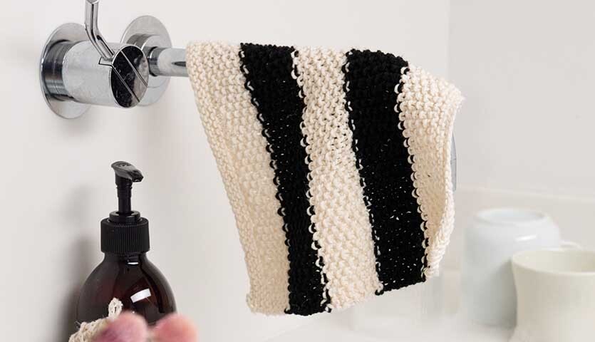 Strickanleitung Spüllappen aus Creative Cotton dk: Schwarz-weiß gestreifter Lappen hängt an einem Wasserhahn im Badezimmer.