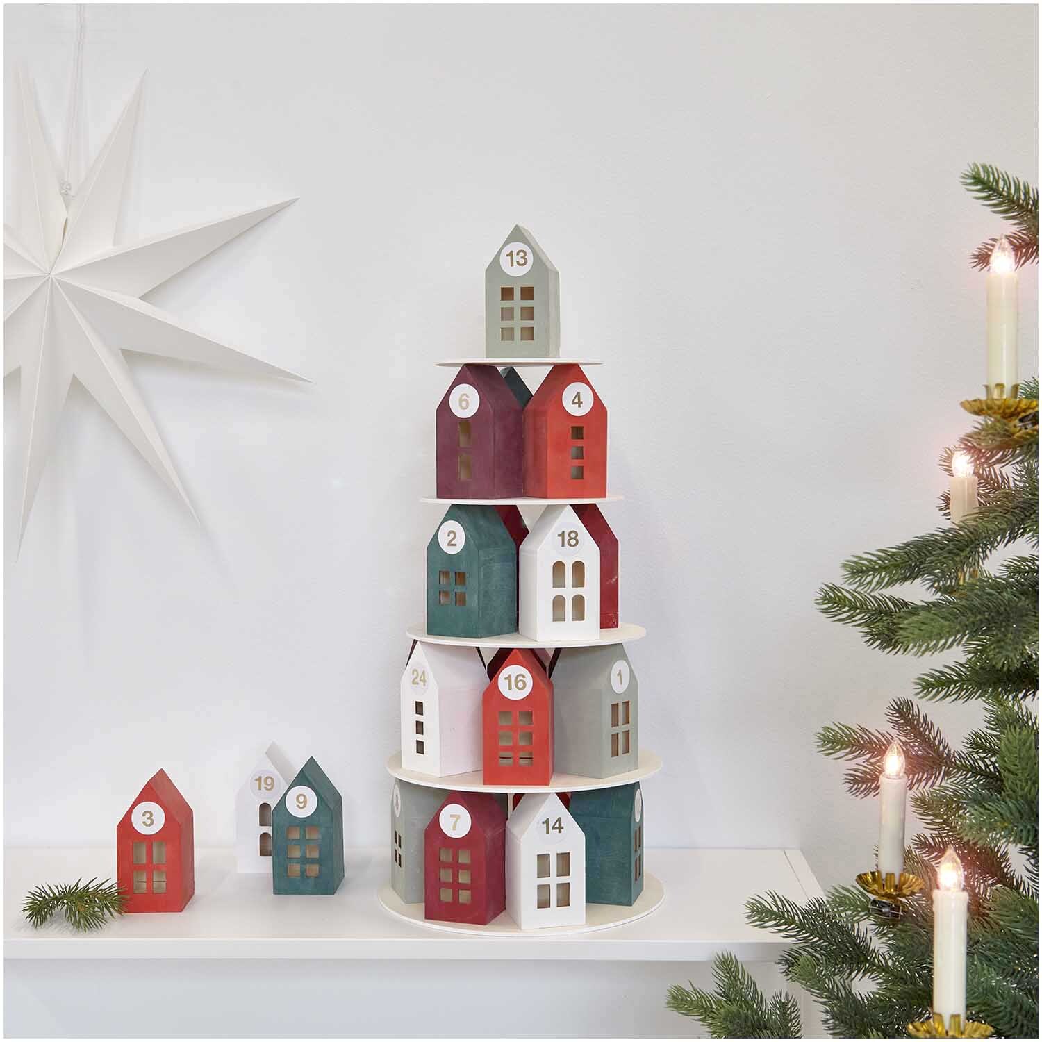 Adventskalender Holz-Haus-Pyramide mit bunten Häuschen, dekoriert neben einem Weihnachtsbaum und Kerzen.