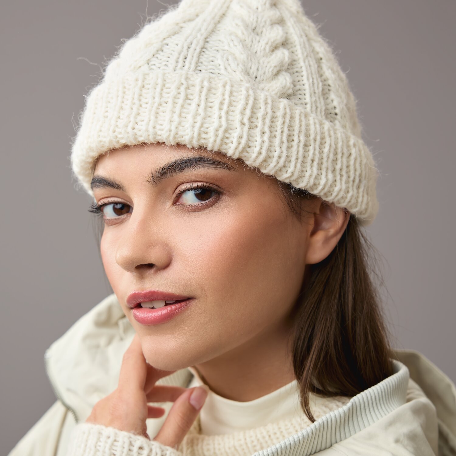 Strickset Mütze Modell 02: Frau trägt cremefarbene Strickmütze mit Zopfmuster, stilvoll kombiniert mit heller Jacke.