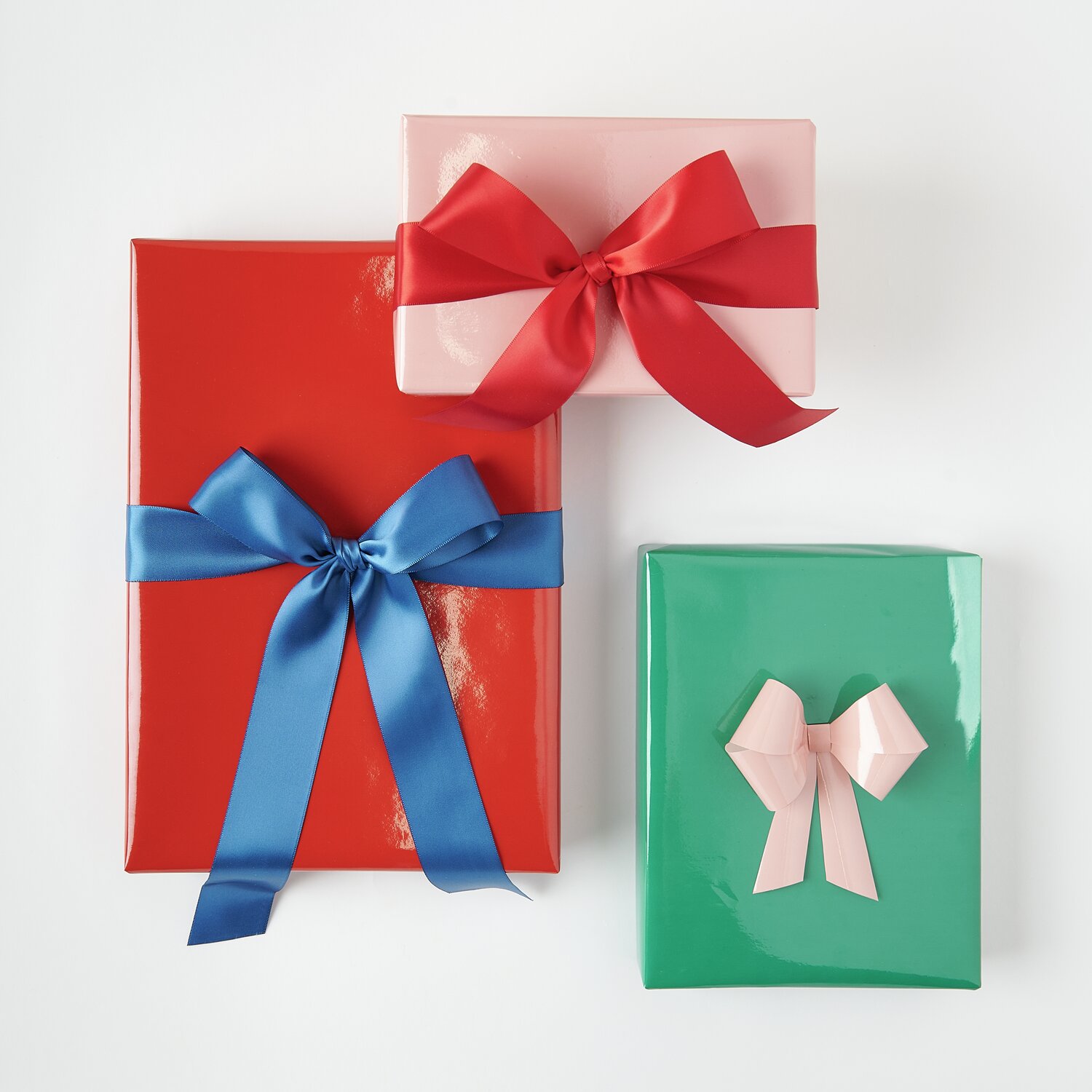 Geschenkpapier Mix Lack Magic Rainbow: Drei glänzende Geschenke in Rot, Altrosa und Dunkelgrün mit farbigen Schleifen von Rico Design.