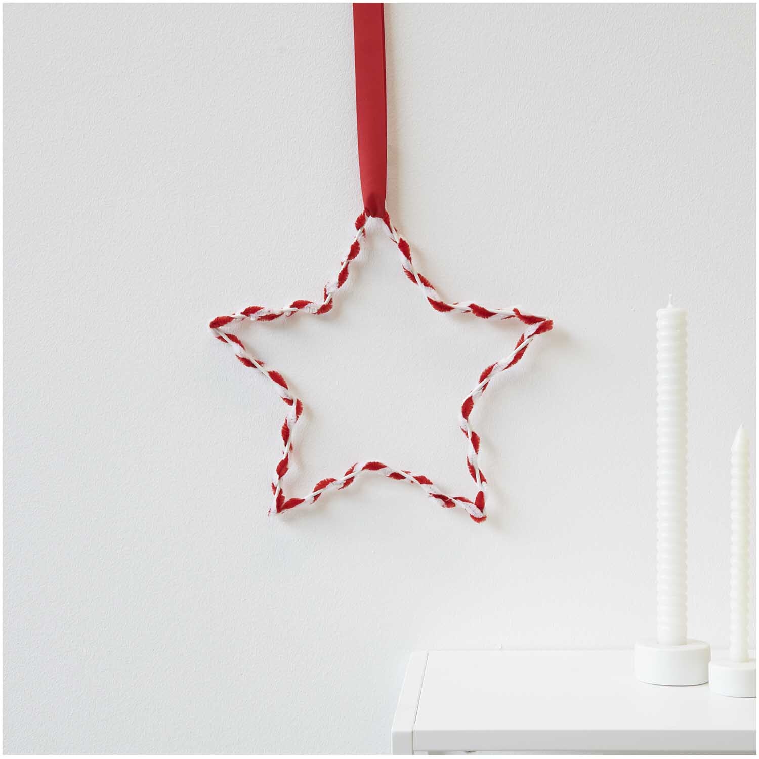 Chenilledraht-Mix 50cm 10 Stück rot & weiß von Rico Design: Sternförmige Dekoration aus rot-weißem Draht, aufgehängt an einer Wand.