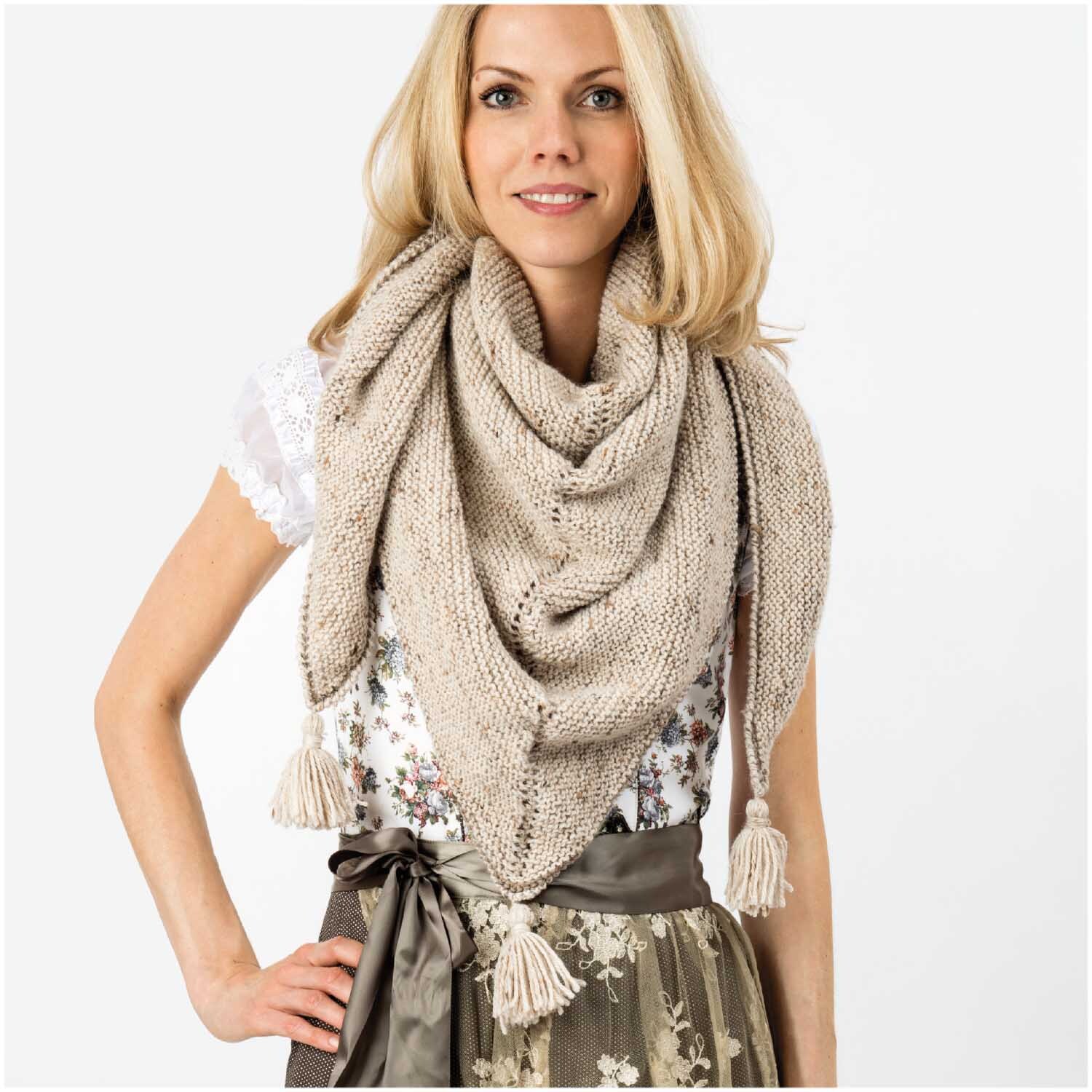 Essentials Merino Plus Tweed dk: Frau trägt beigen Strickschal mit Fransen, kombiniert mit floraler Bluse.