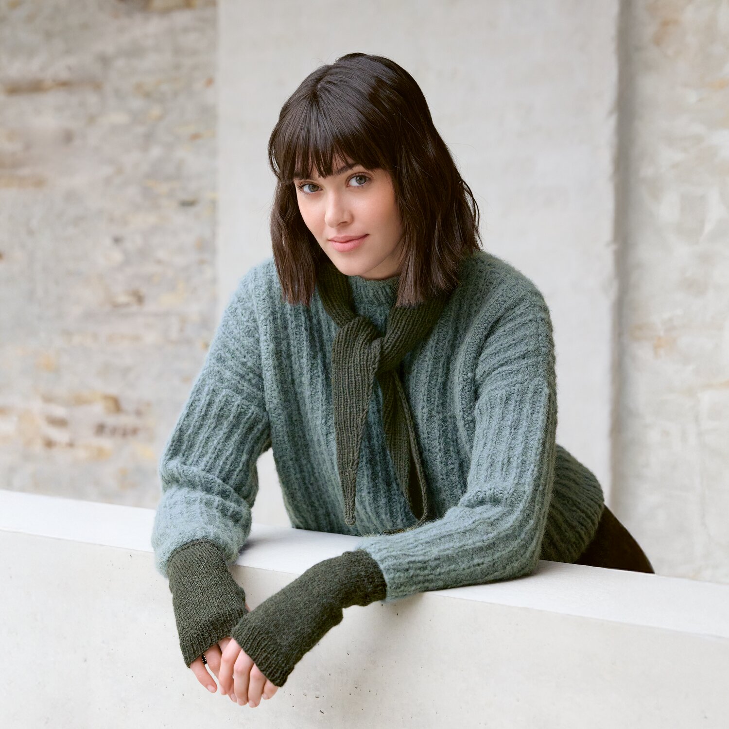 Strickset Mini-Dreieckstuch Modell 13: Frau trägt grünen Pullover und Schal aus Luxury Knits.