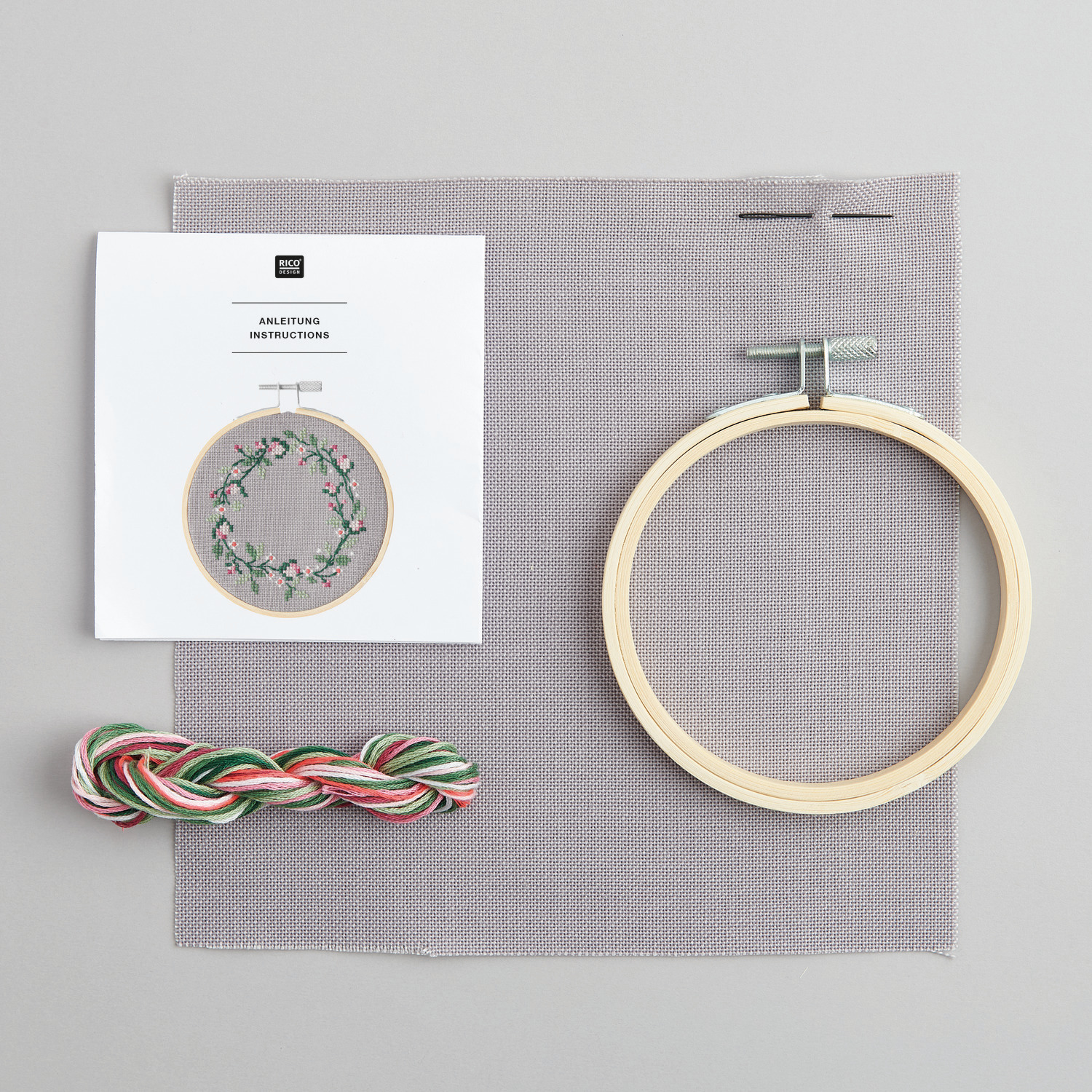 Stickpackung Bild Blumenkranz mit Holzrahmen, Garn und Anleitung auf grauem Stoff von Rico Design. Ideal für kreative Handarbeiten.
