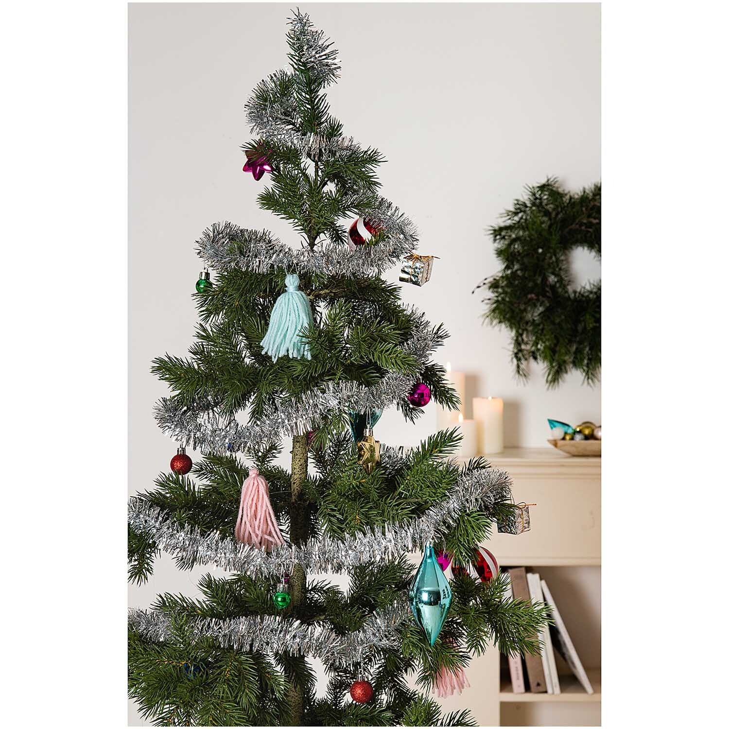 Girlande Lametta mit Dekor 2,5m schmückt einen Weihnachtsbaum mit buntem Schmuck und Lametta. Im Hintergrund sind Kerzen und ein Kranz zu sehen.