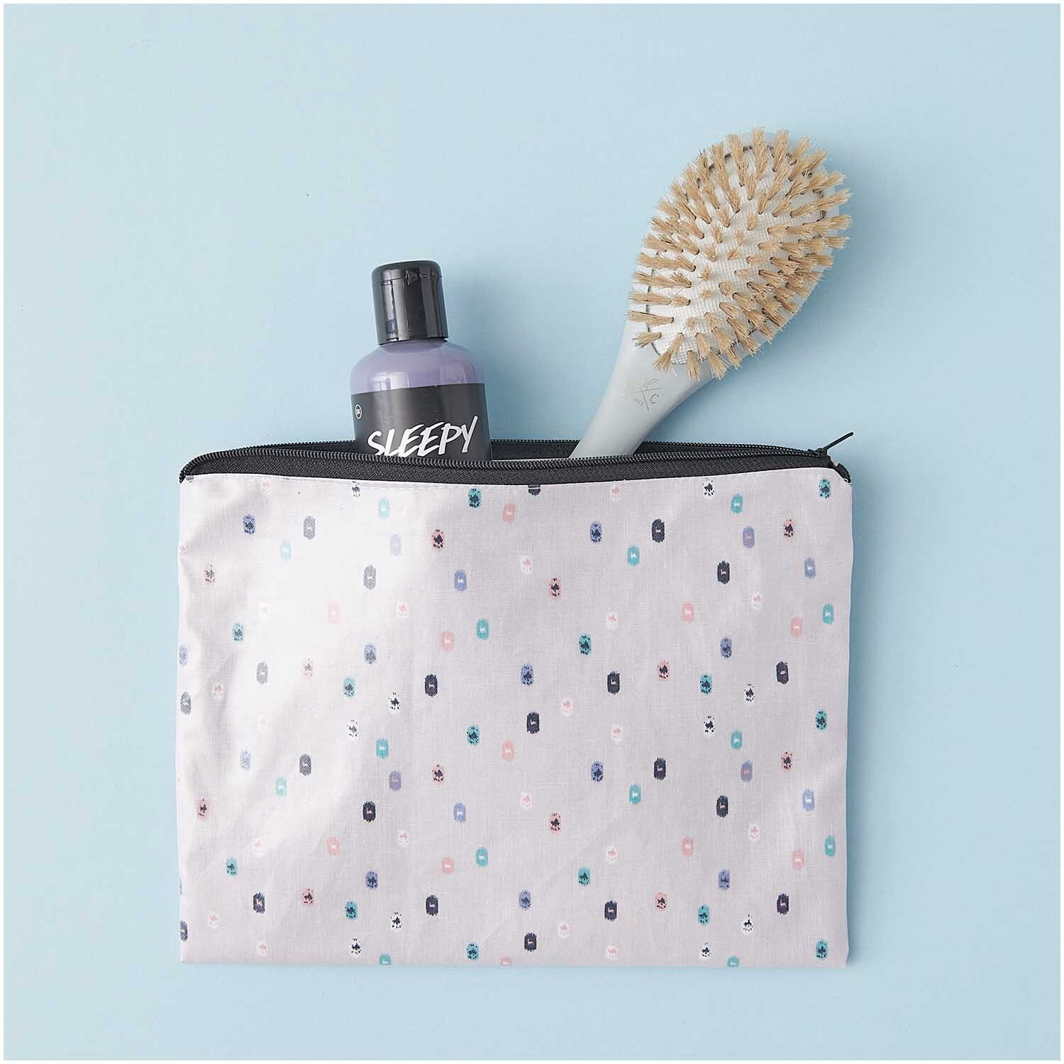 Pouch Travel the World flieder 17x23cm mit Fläschchen und Bürste auf hellblauem Hintergrund.