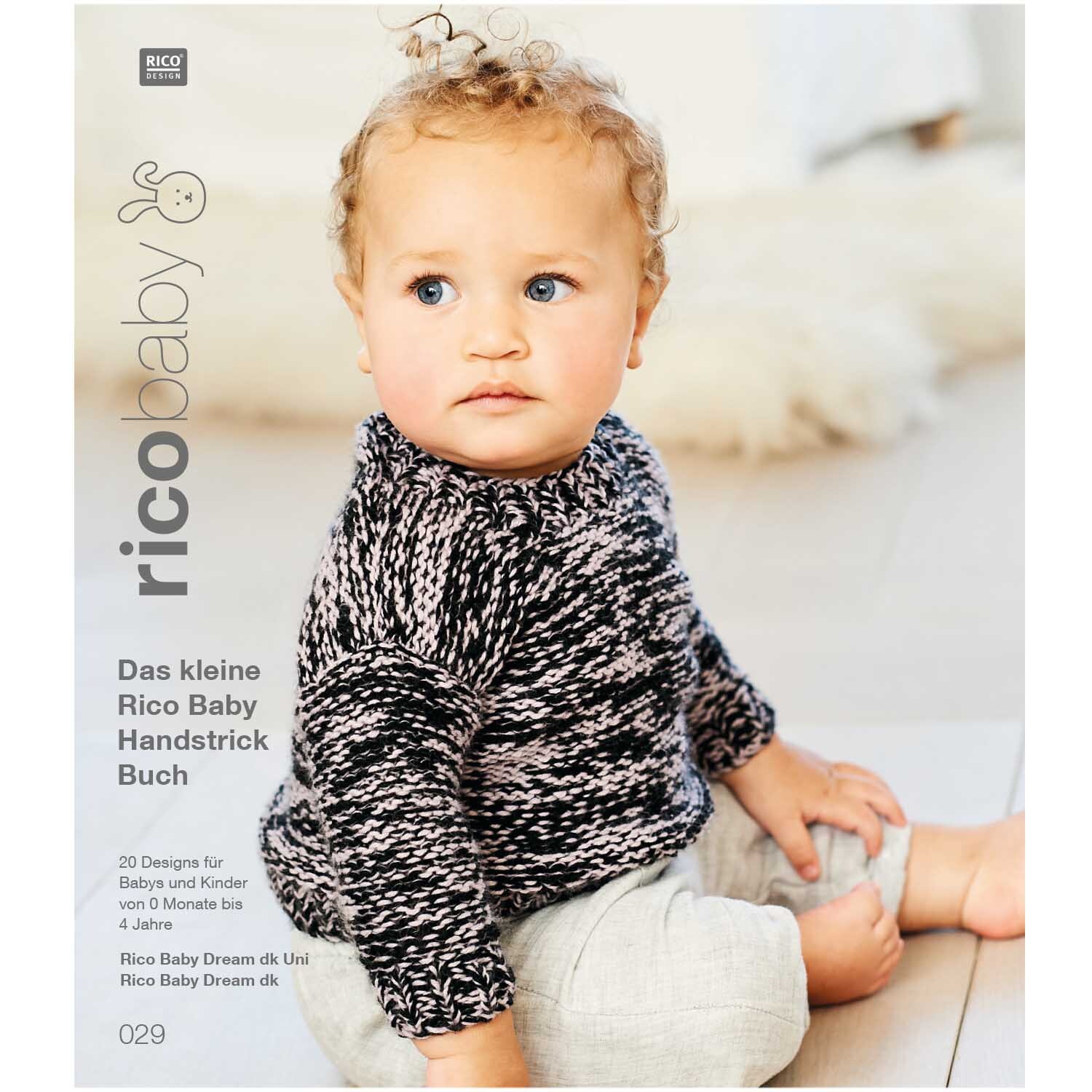 Rico Baby Heft Nr.29 zeigt ein Baby in einem schwarz-weiß gestrickten Pullover auf einem Holzboden.