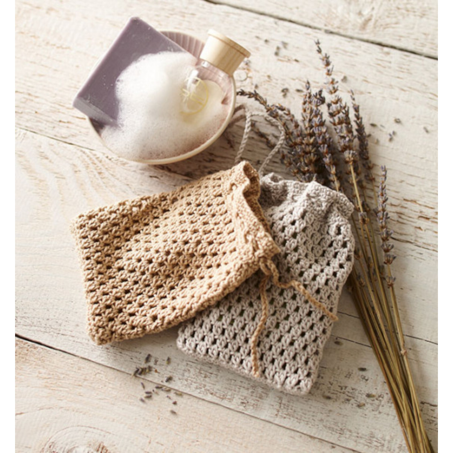 1x1 Häkeln - Grundwissen, Modelle & Inspirationen: Zwei gehäkelte Beutel in Beige und Grau auf Holzuntergrund mit Lavendel und Seifenschale.