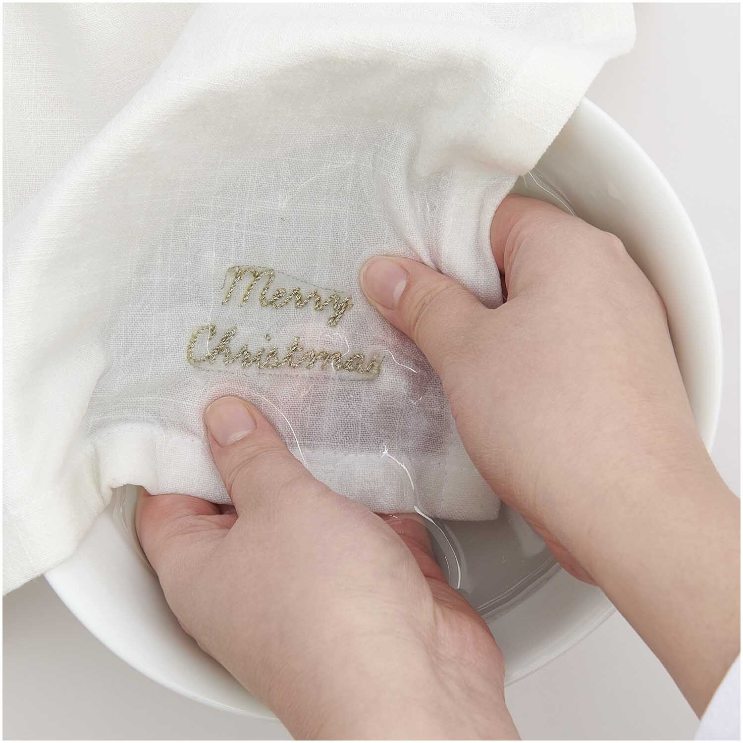 Stick and Stitch Stickpackung Merry Christmas vorgezeichnet: Hände halten ein weißes Tuch mit gesticktem "Merry Christmas" von Rico Design.