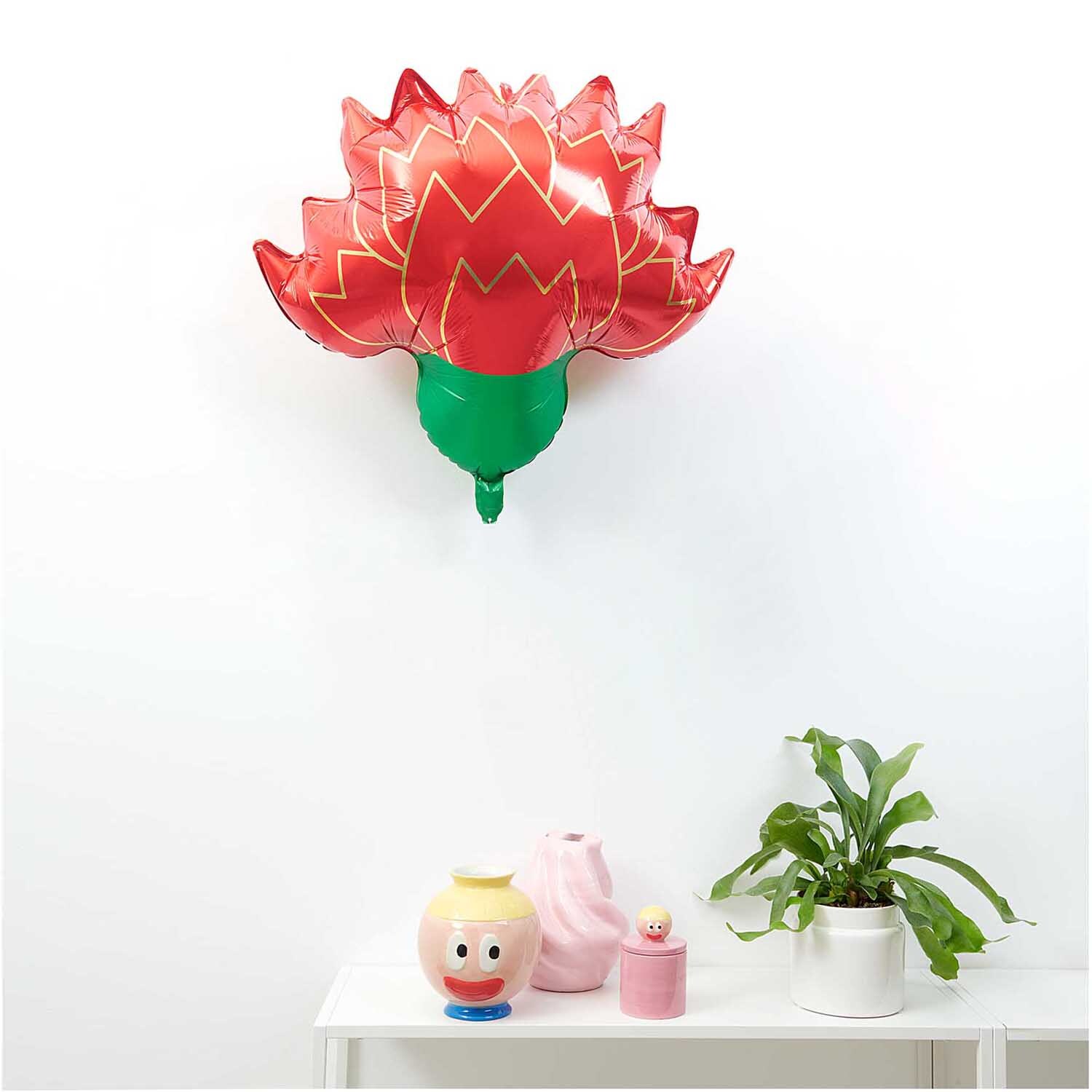 Rico Design x Redfries Folienballon Nelke in Rot und Grün schwebt über einem weißen Tisch mit Dekoration.