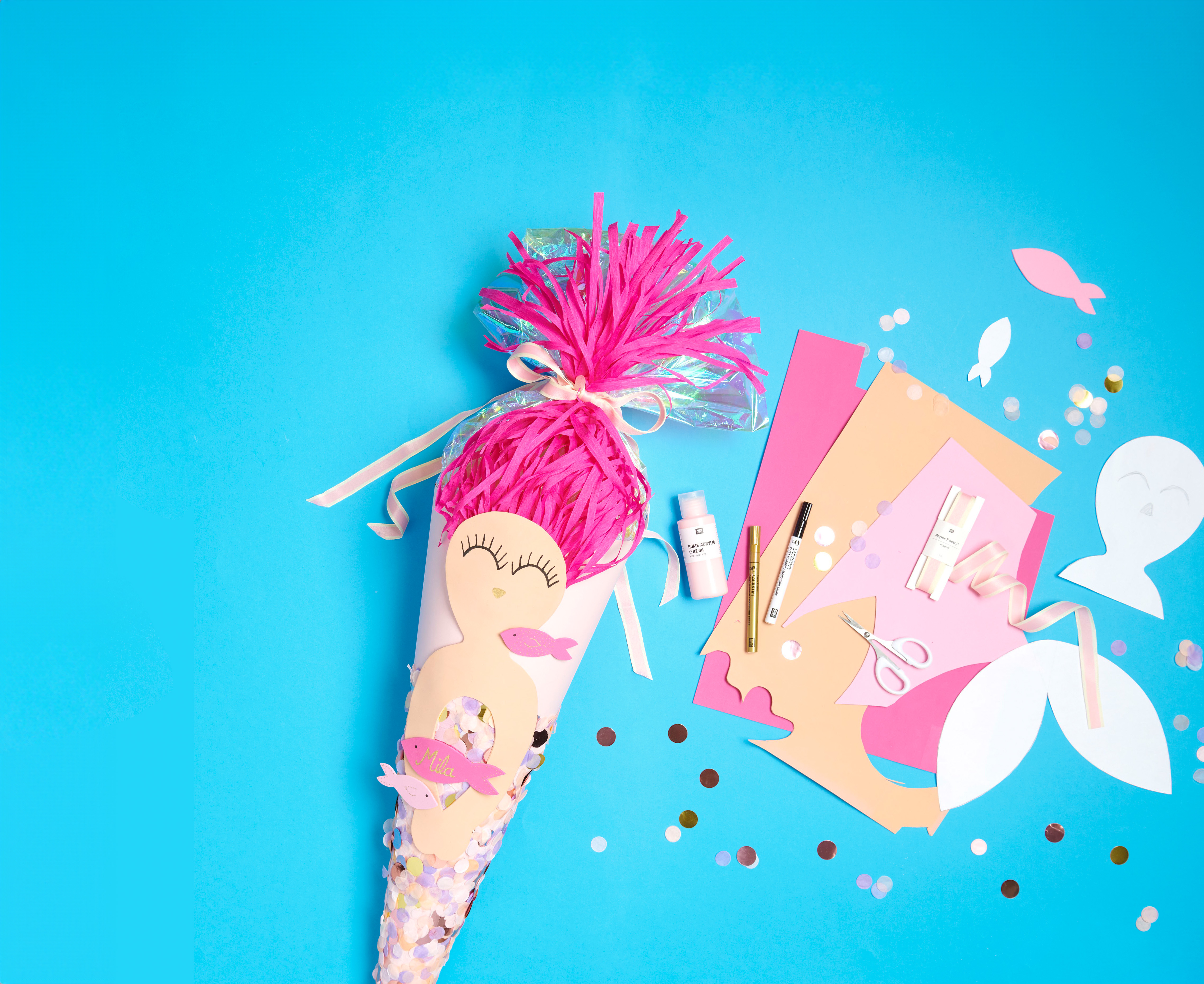 Schultüte mit pinkem Meerjungfrauen-Motiv und daneben dazugehöriges Bastelmaterial. Flatlay von Produkten.