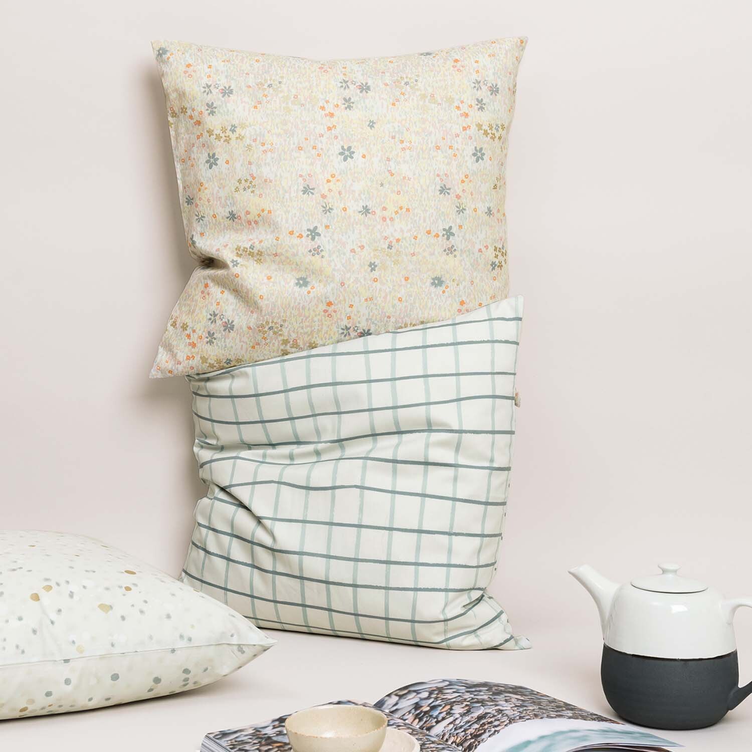 Nähanleitung Kissenbezüge aus Crafted Nature Stoffen: Zwei Kissen mit floralen und karierten Mustern, arrangiert neben einer Teekanne.